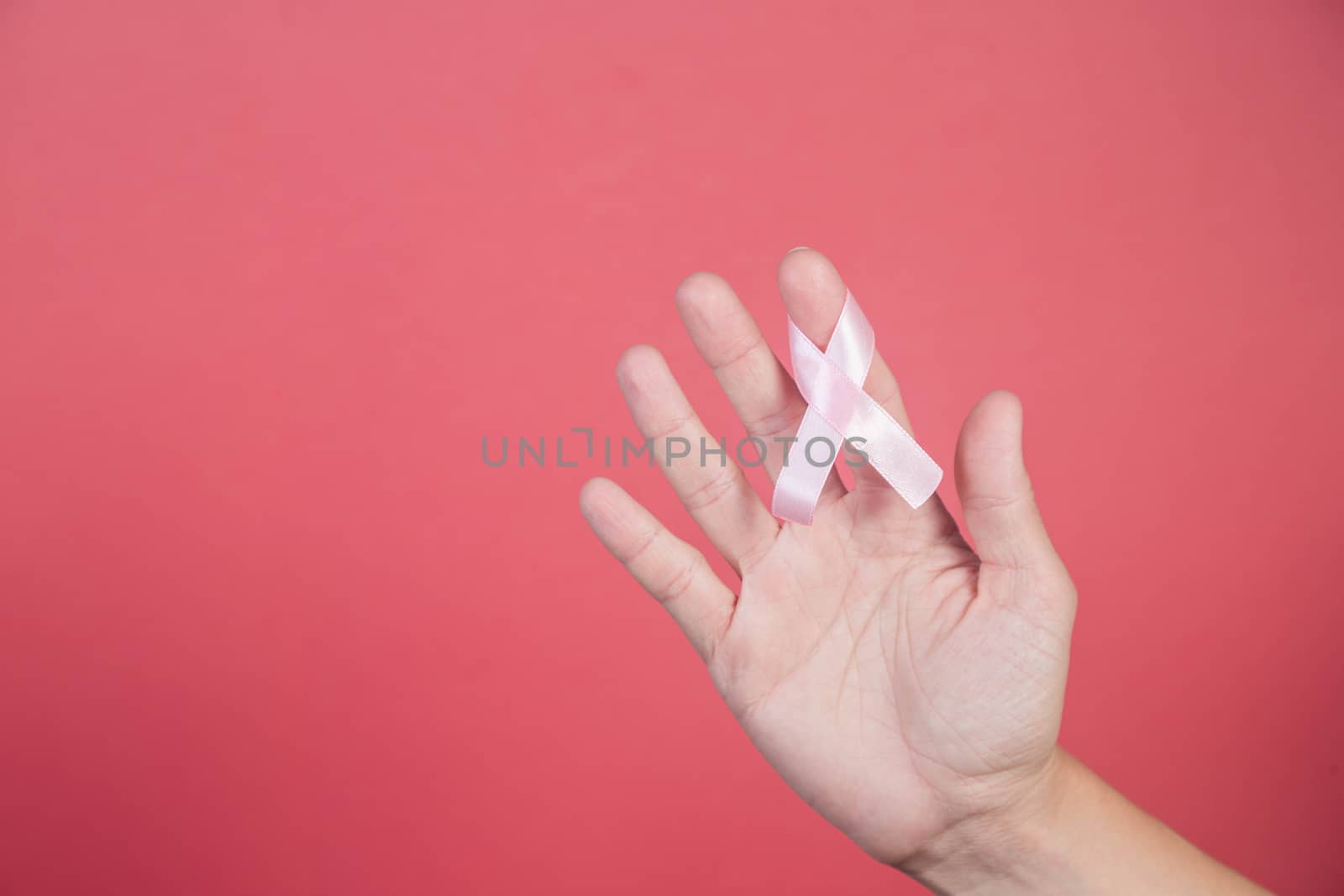 Pink ribbon in a woman hands on pink background. by galinasharapova