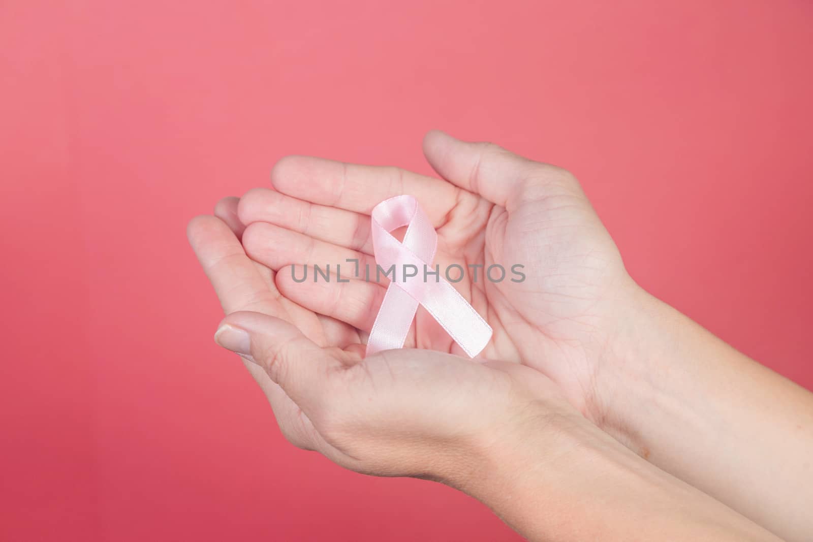 Pink ribbon on a woman hands on pink background. Breast cancer, healthcare and medicine concept, symbolic tape