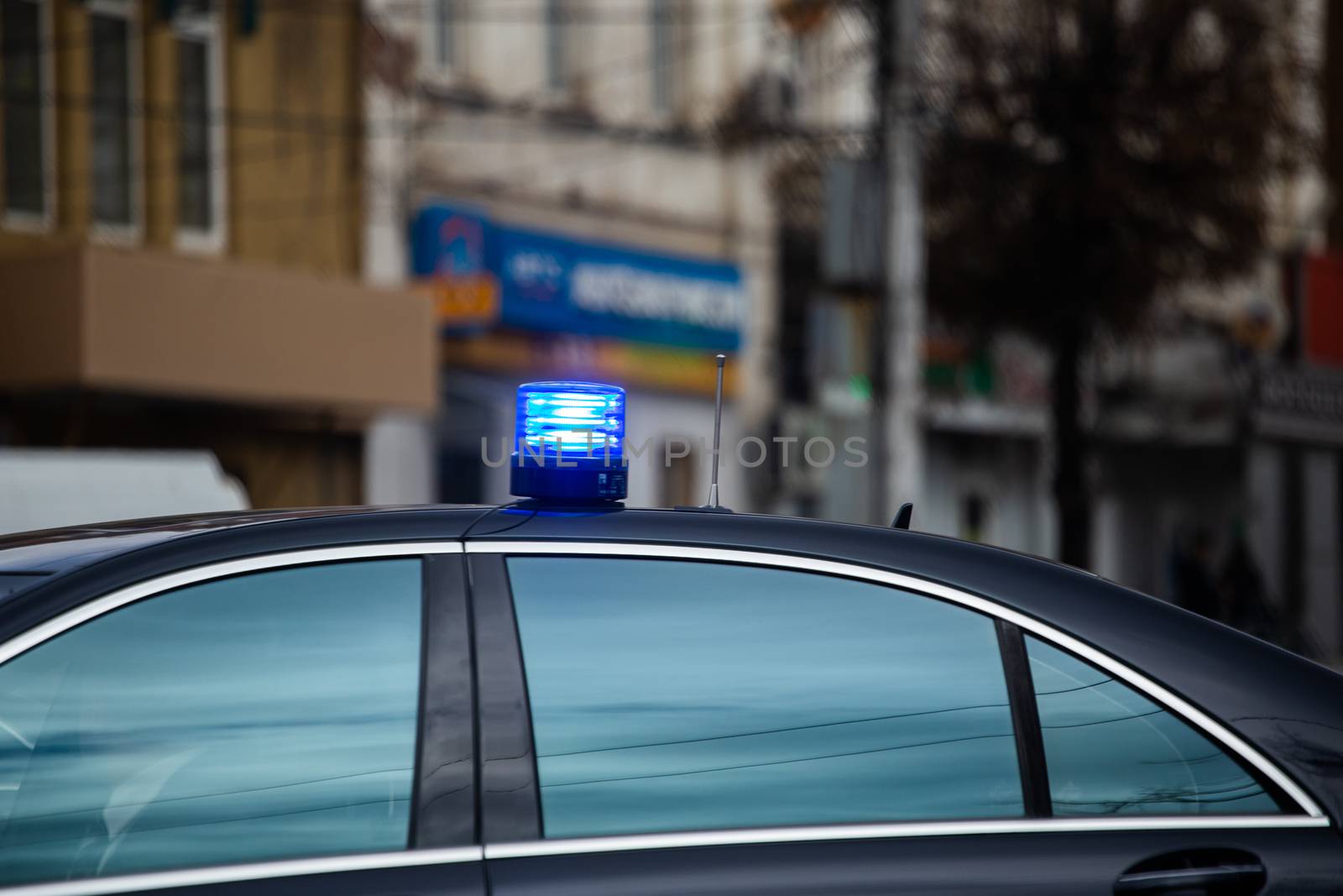 blue flashing light on top of black government car on daytime city street.