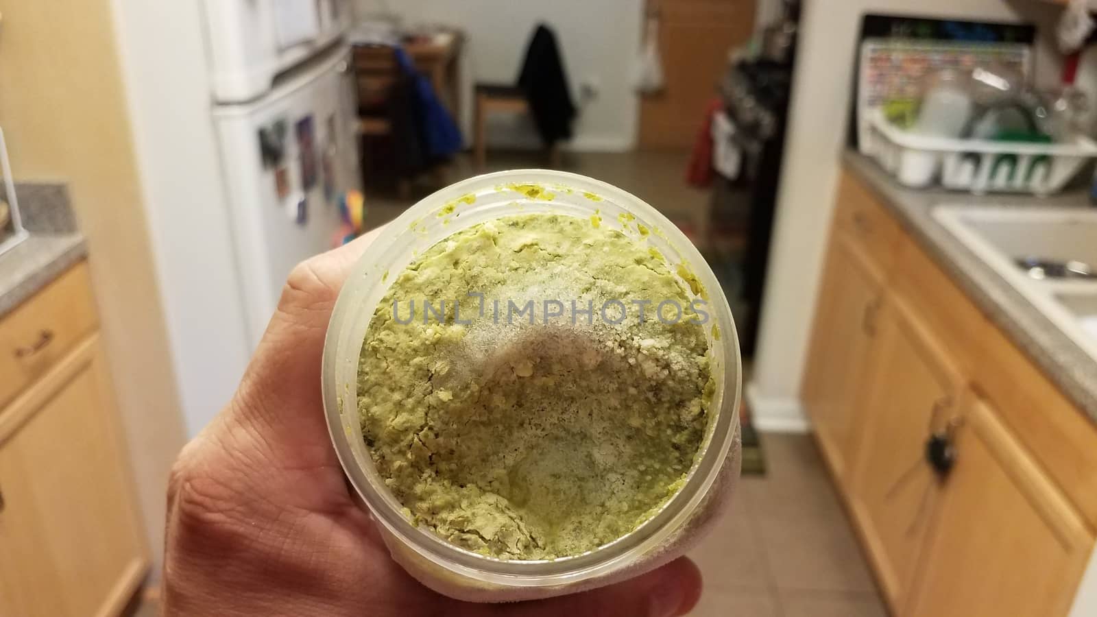 hand holding container of green pesto sauce with ice in kitchen by stockphotofan1