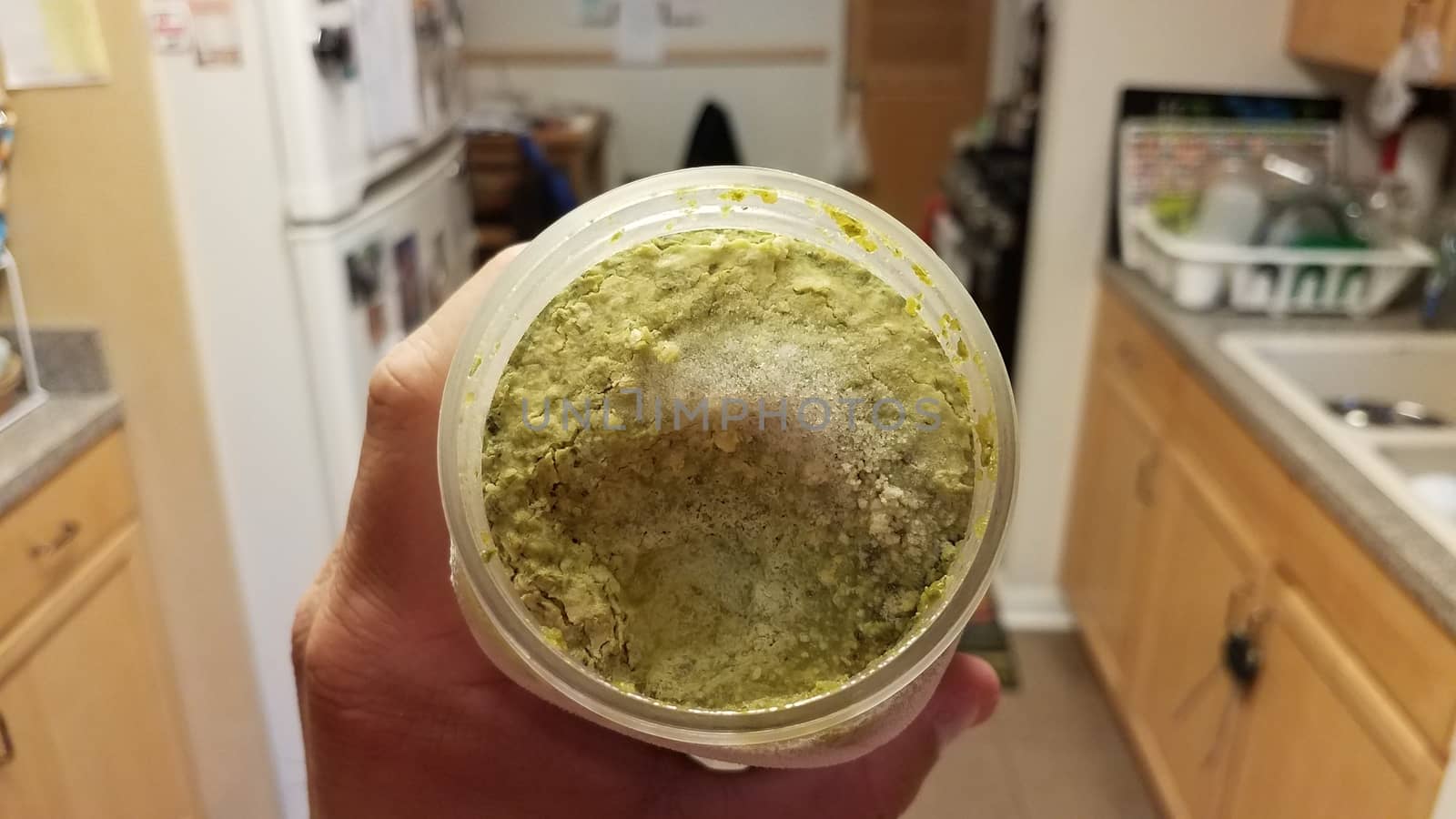 hand holding container of green pesto sauce with ice crystals in kitchen