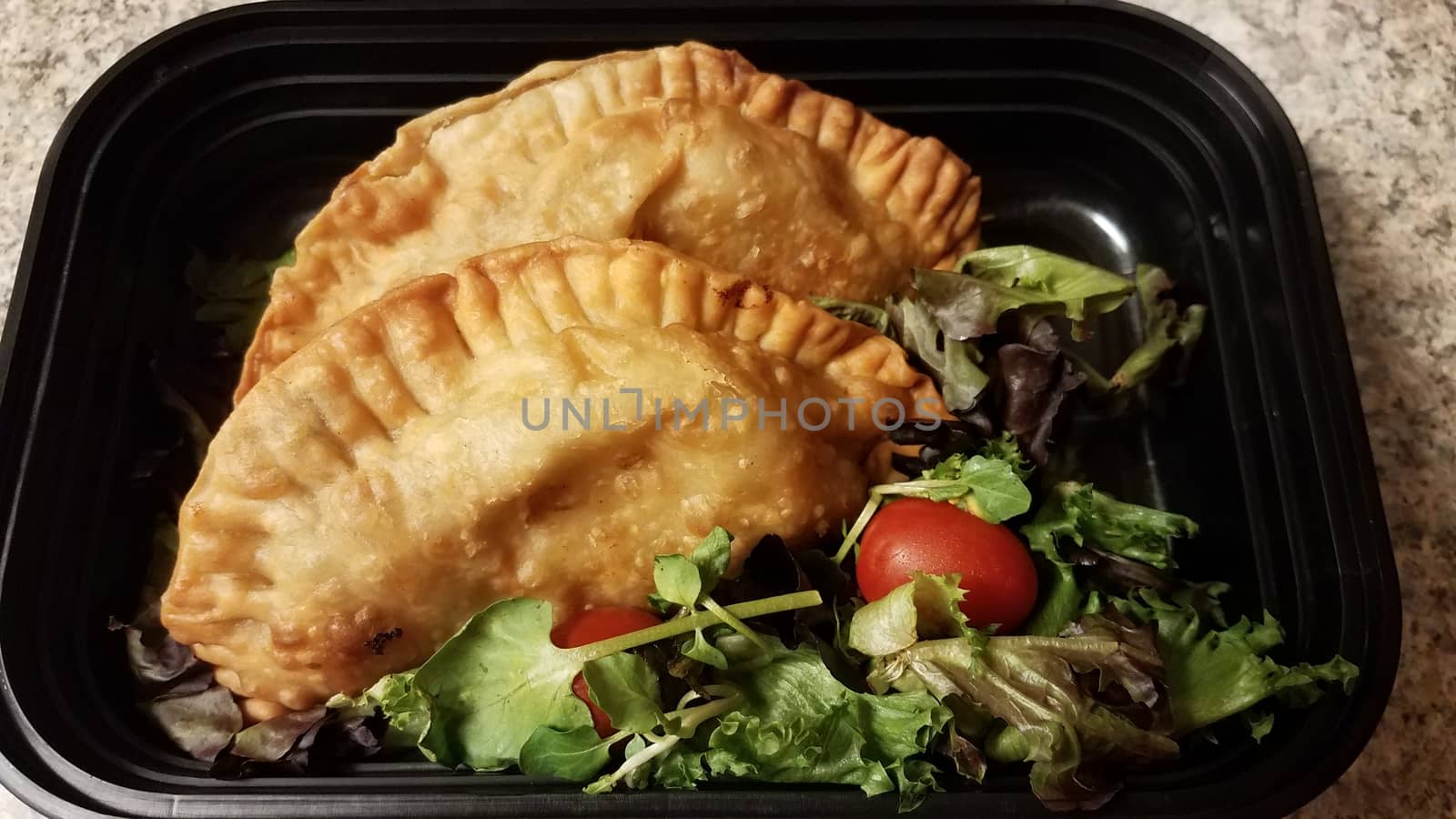 Puerto Rican fried beef turnover and salad in container on counter