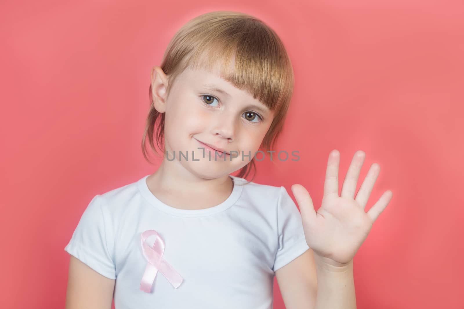 Little girl showing stop sign with hand wearing white t-shirt and pink breast cancer awareness ribbon