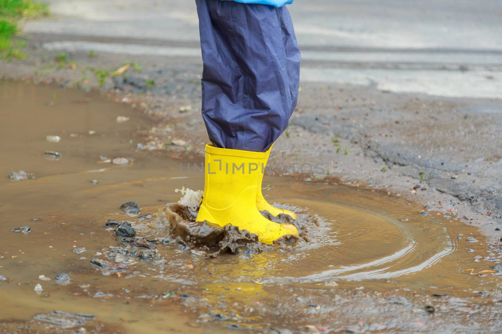 Feet of child in yellow rubber boots jumping over puddle in rain by galinasharapova