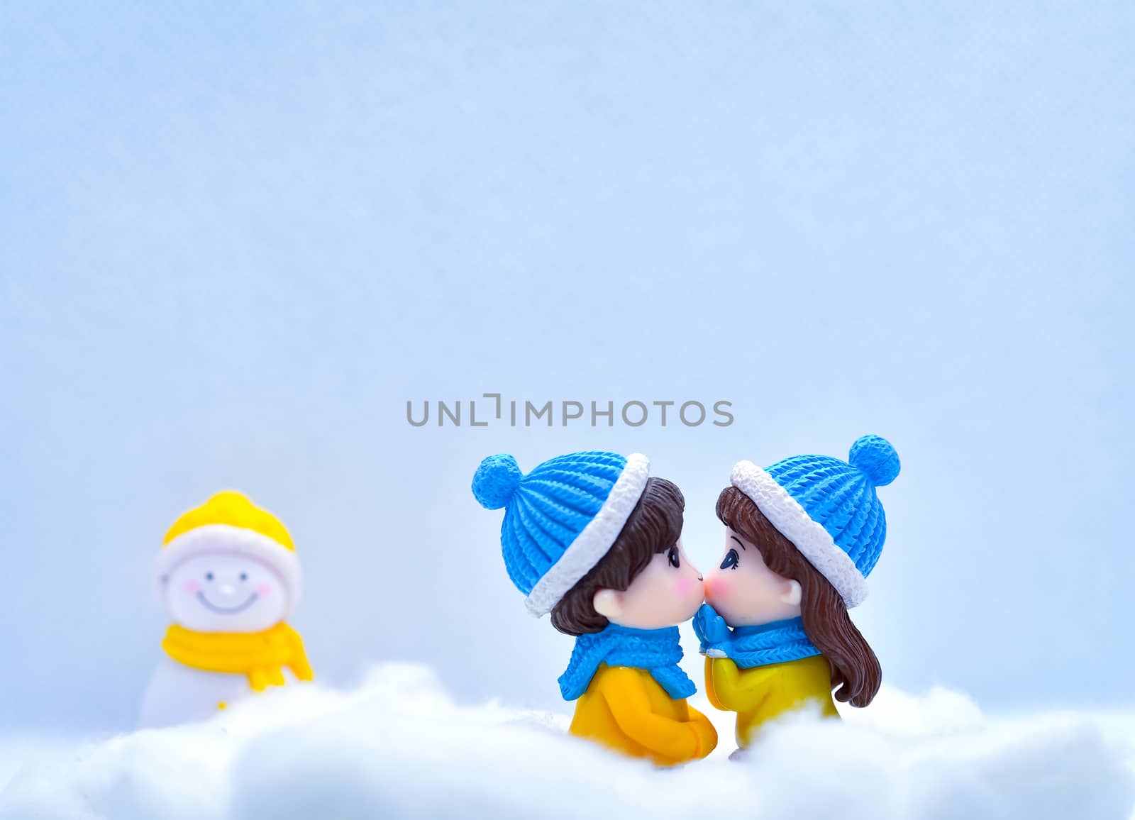 Tourism and travel concept: Miniature people kissing each other in winter snow with little snowman in the background