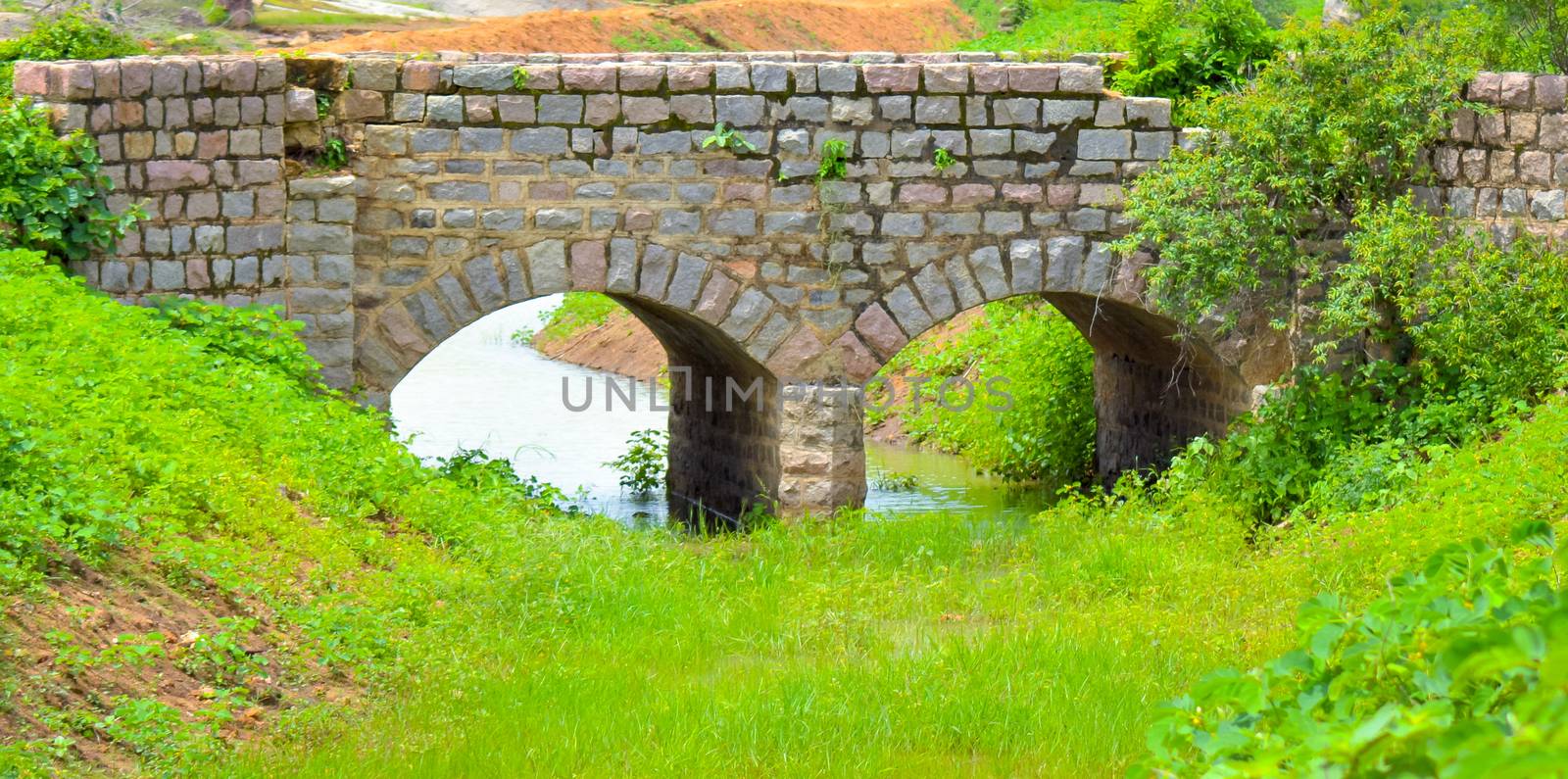 Old stone single arch bridge, Latvia. Famous ancient stone arch single track road bridge in the forest. View of small river and trees reflection in the water.