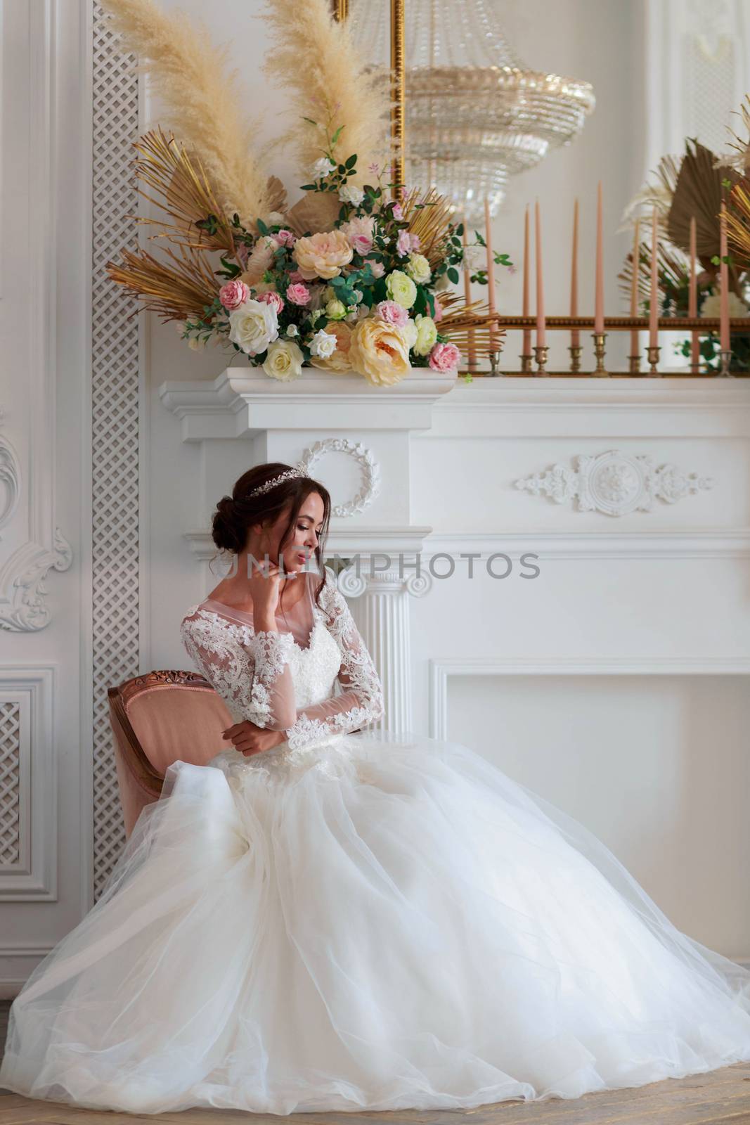 The bride in a white wedding dress sits thoughtfully in a chair waiting for the groom.