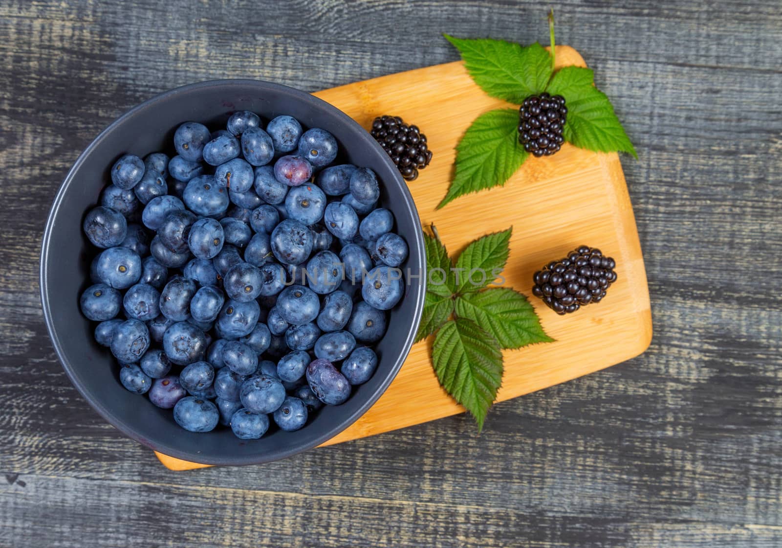 blueberry berry in dark gray ceramic bowl on wooden cutting board on dark blue wooden background. top view soft focus