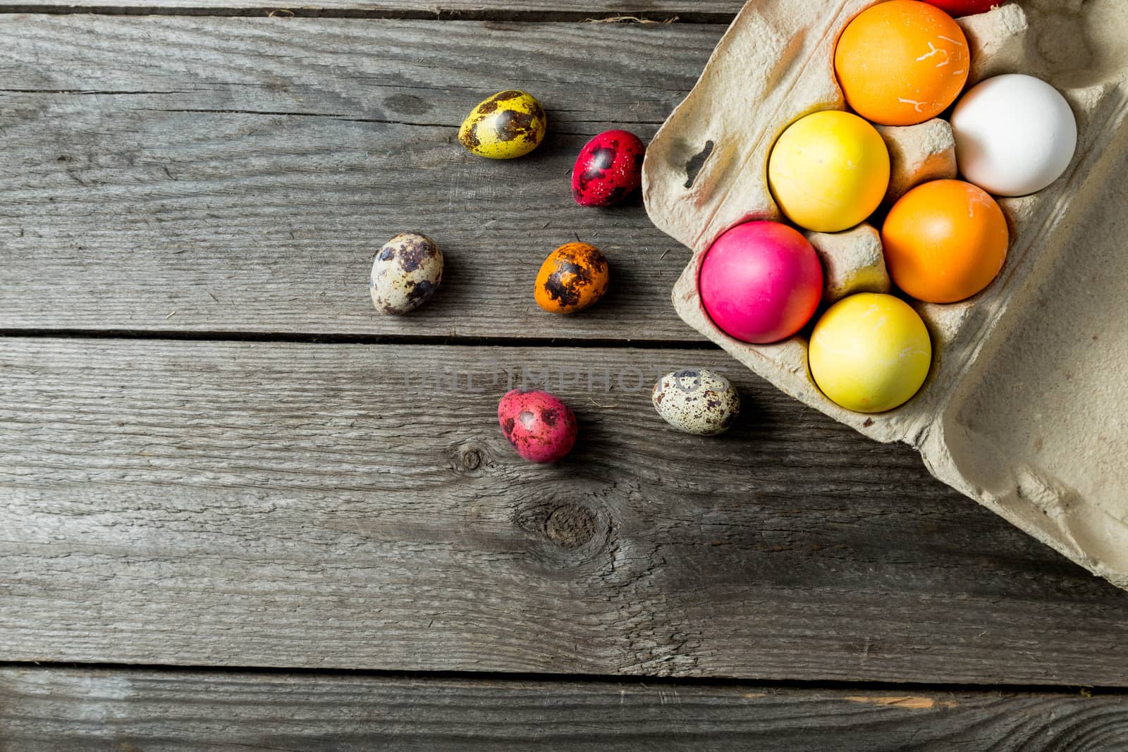 Dyed easter eggs in cardboard box on wooden background. Easter background with space for a text.