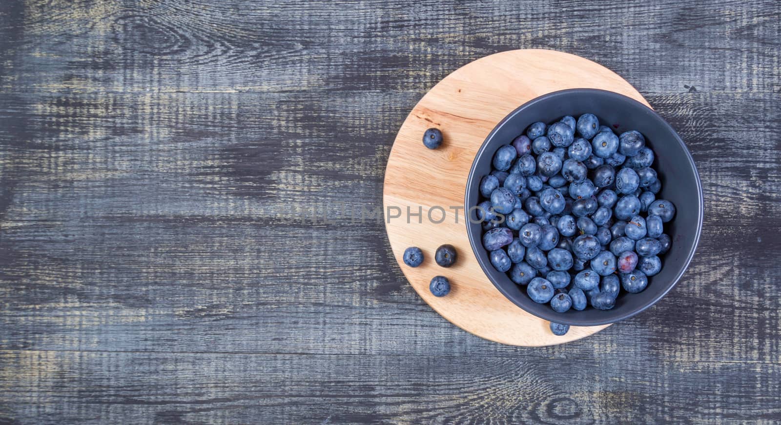 blueberry berry in dark gray ceramic bowl on wooden cutting board on dark blue wooden background.Banner, place for text.