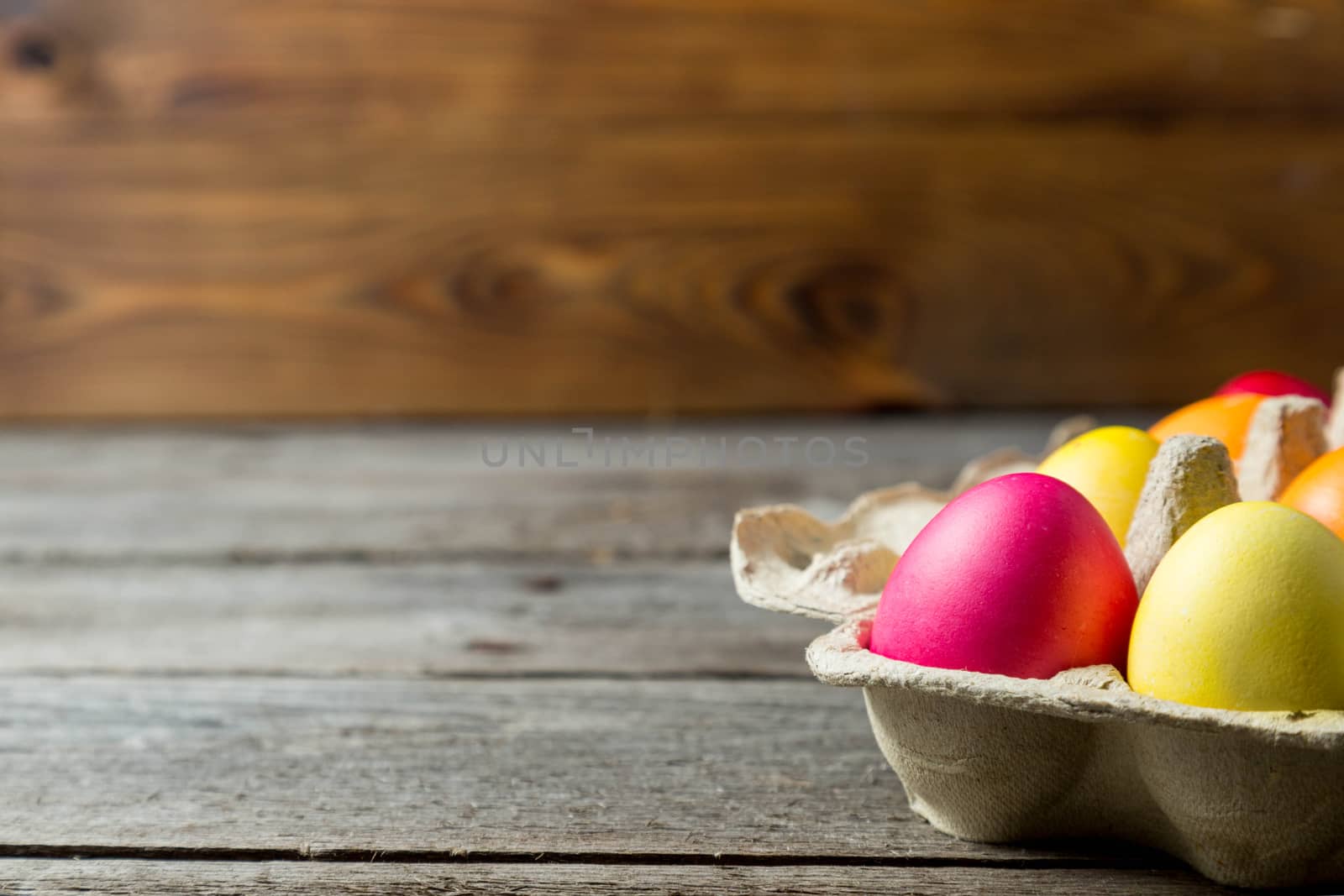 Dyed easter eggs in cardboard box on wooden background. Easter background with space for a text.