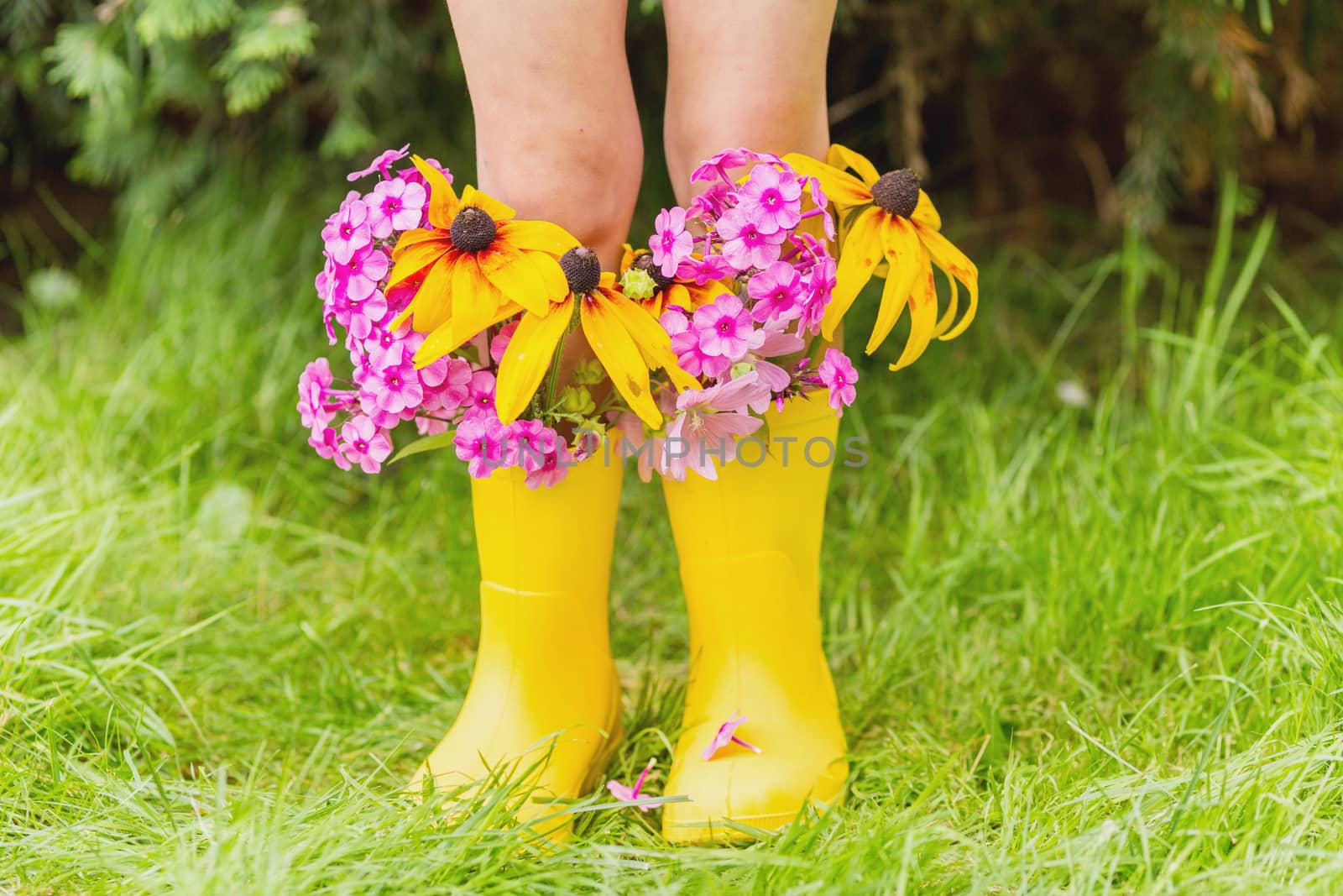 Child's feet in rubber yellow boots with autumn flowers in it