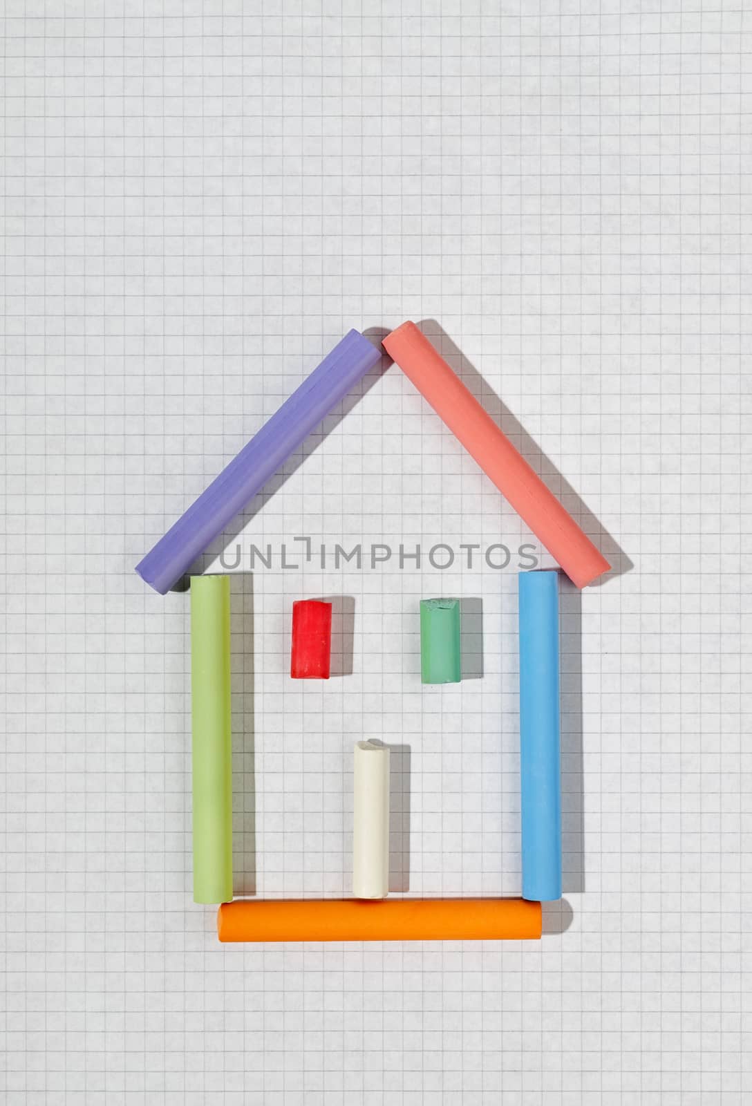 Colorful house shape with different pieces of chalk on white squared notebook sheet