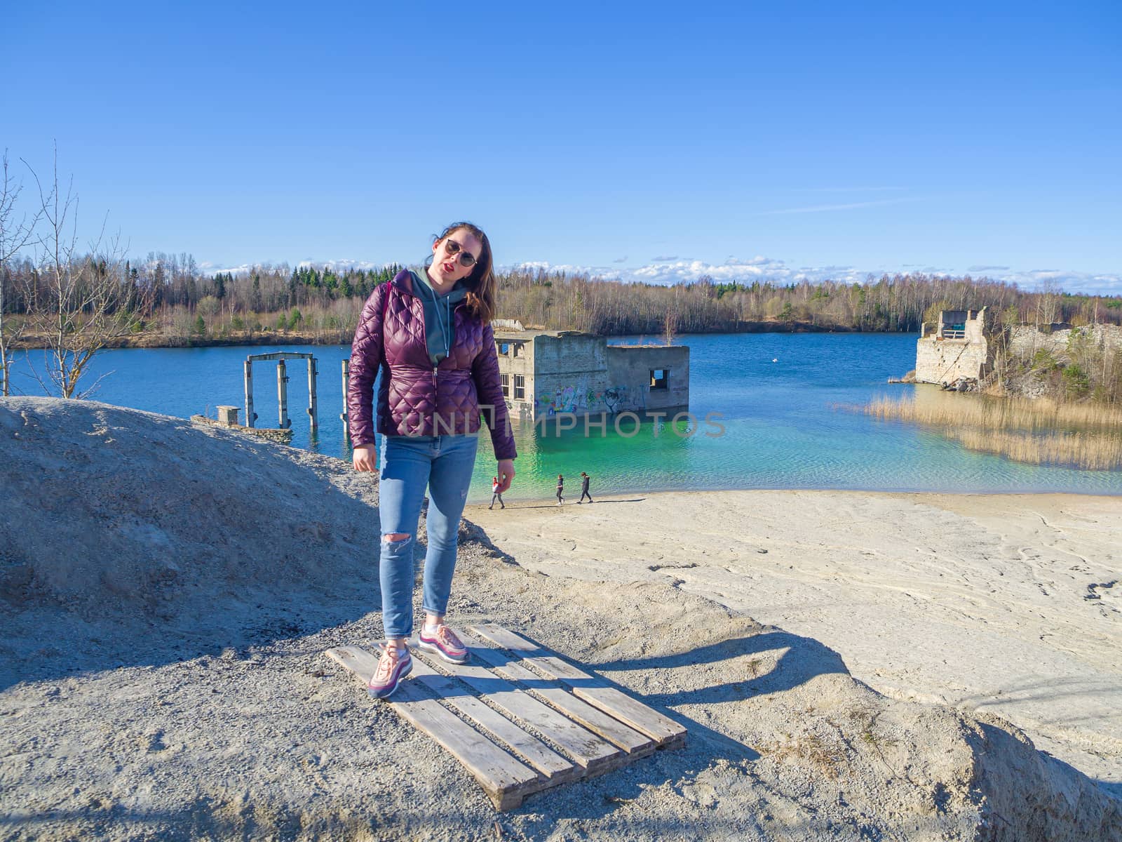 Hiker on mountain top. Woman is standing with an Abandoned Quarry and water on the background. Scenic View Of Land Against Clear Blue Sky. Panoramic View.