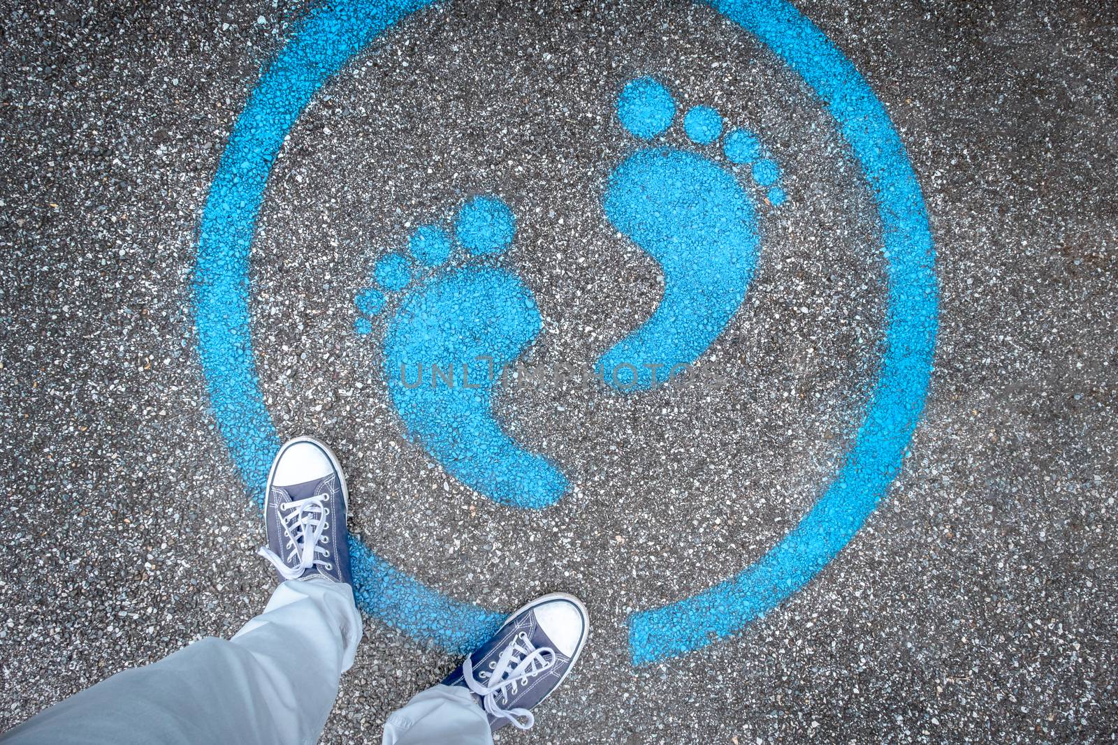Man standing on blue dot. Sign painted on the pavement reminding users to maintain a physical distance of 3 feet / 1 meter during the COVID-19 pandemic.