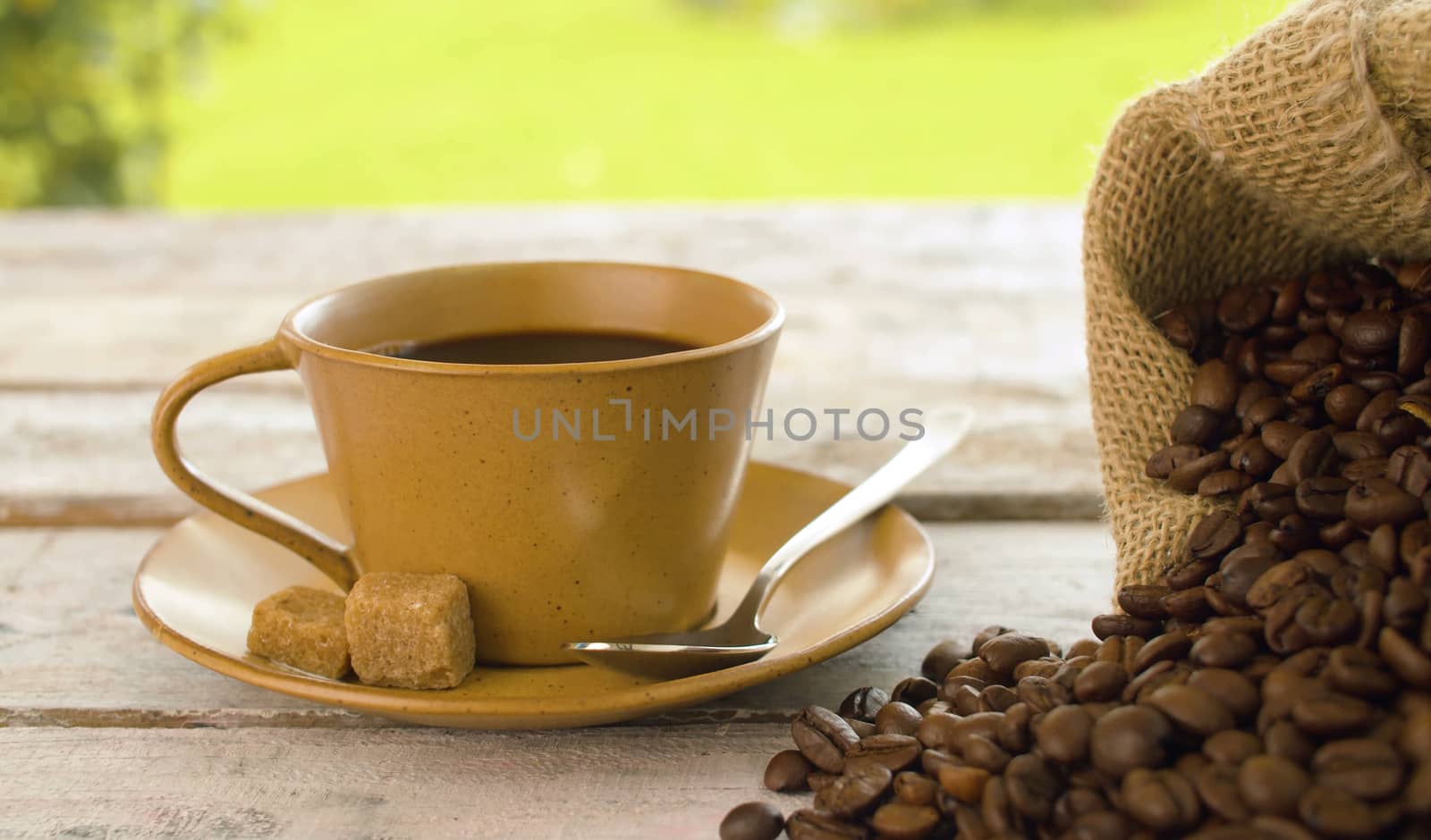 Close-up of coffee beans in a burlap jute sack and cup of coffee on a wooden table outdoors. Dolly shot