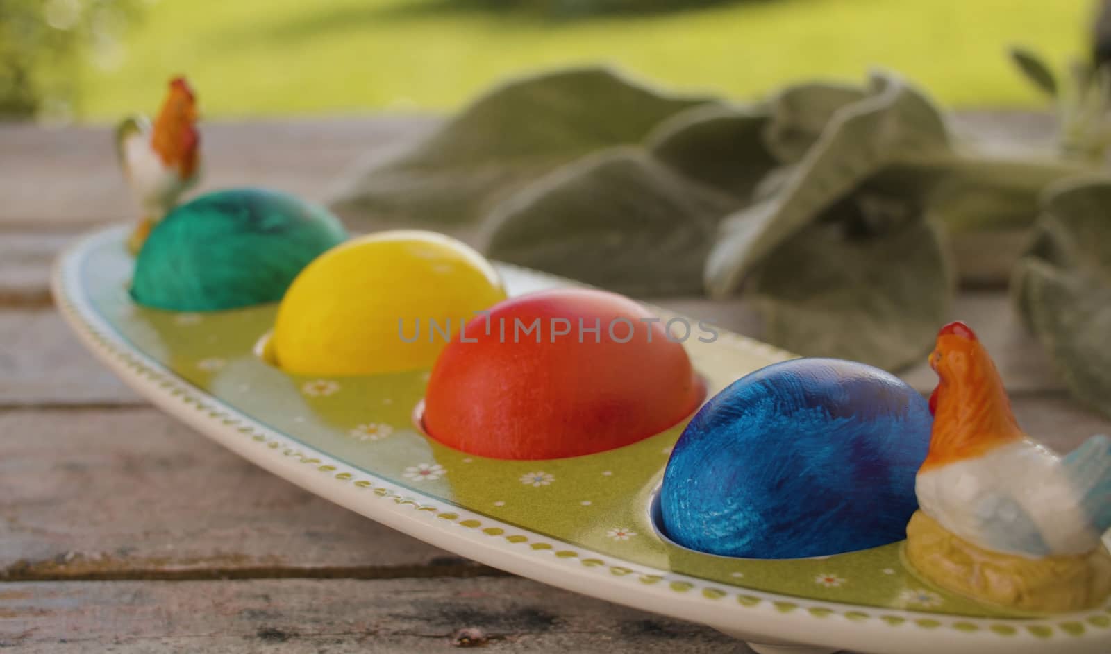 Close up multicolored painted Easter eggs in egg box and rabbits ear plant on wooden table in the garden. Holiday concept