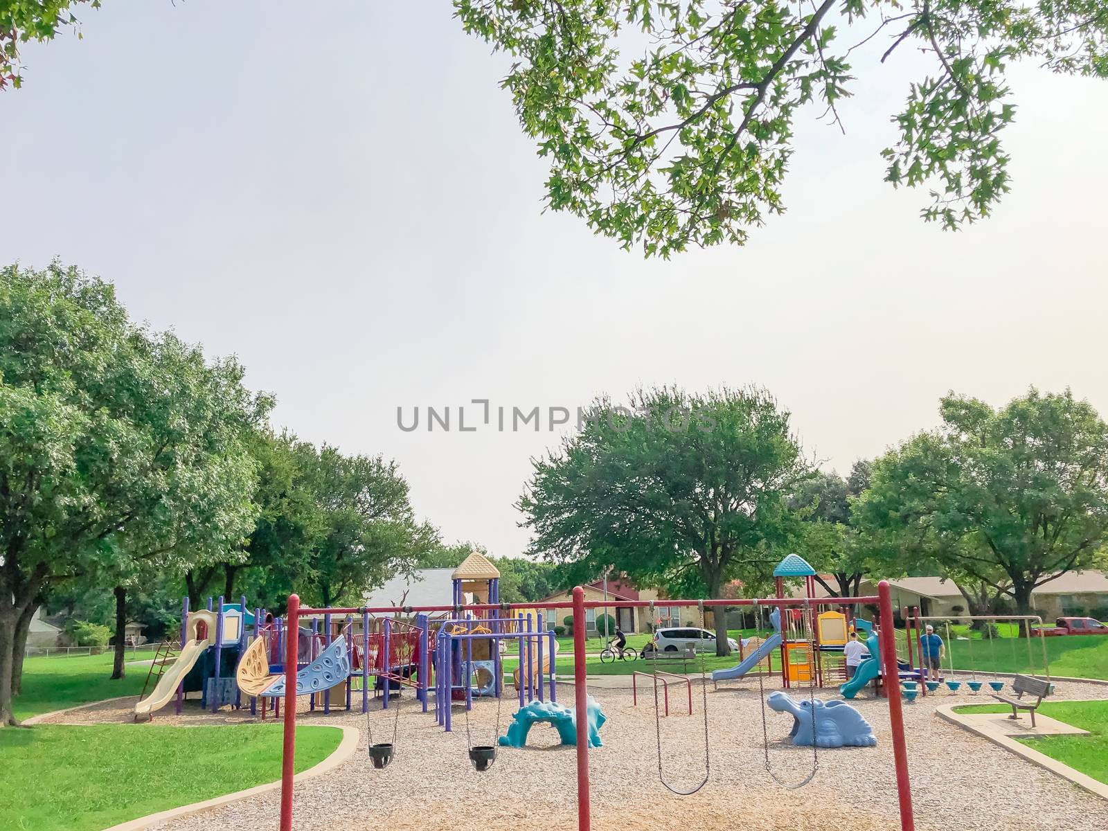 Swing set at large playground in residential neighborhood near Dallas, Texas, America. Community park with row of single family houses in background