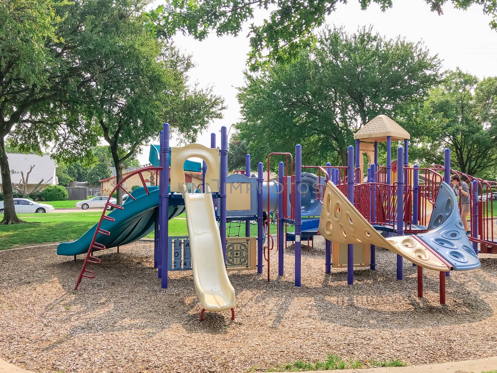 Variety of slide and swing at Colorful playground near residential neighborhood in Richardson, Texas, America. Community facility surrounded by large oak trees and green grass lawn