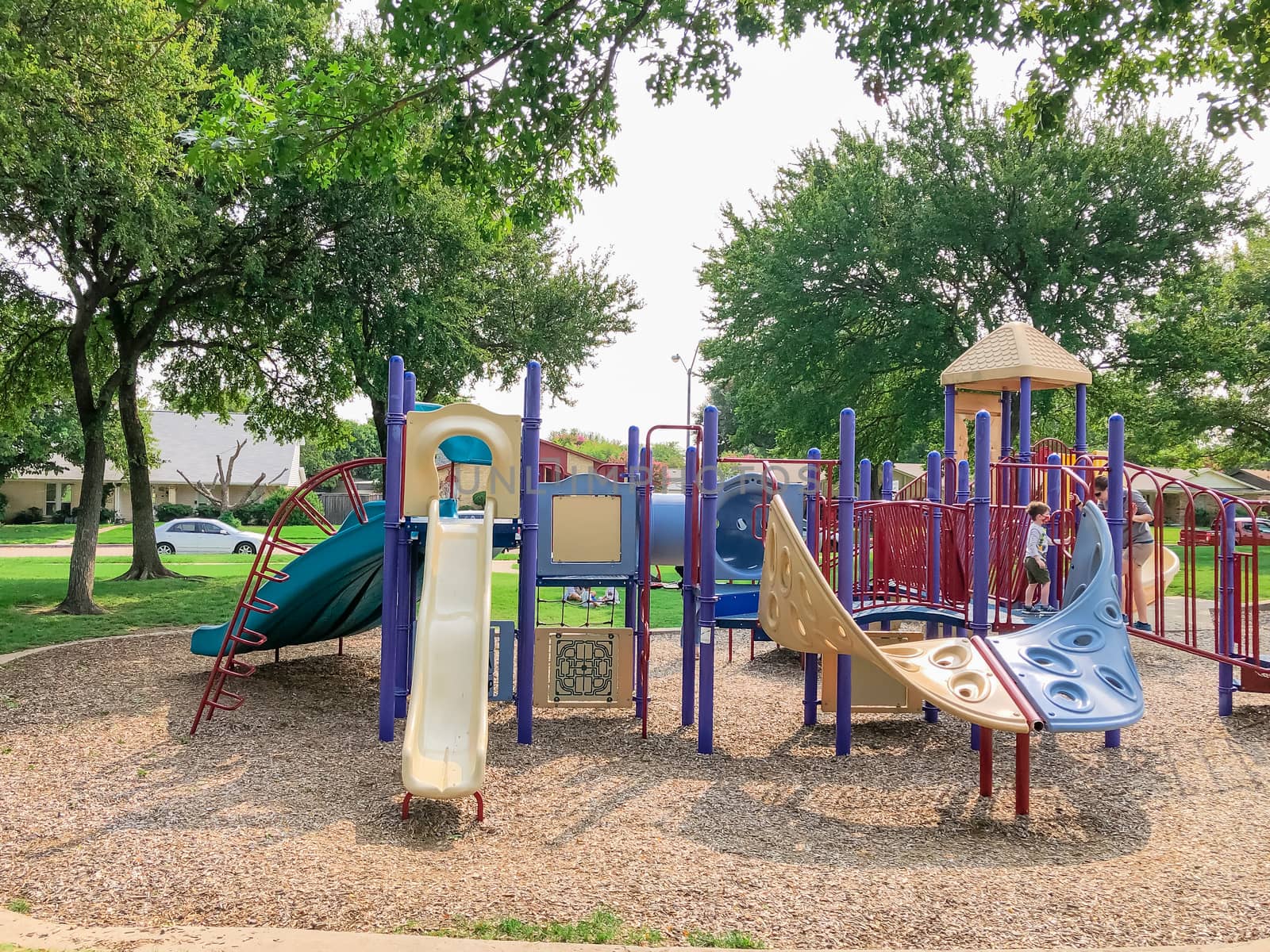 Variety of slide and swing at Colorful playground near residential neighborhood in Richardson, Texas, America. Community facility surrounded by large oak trees and green grass lawn