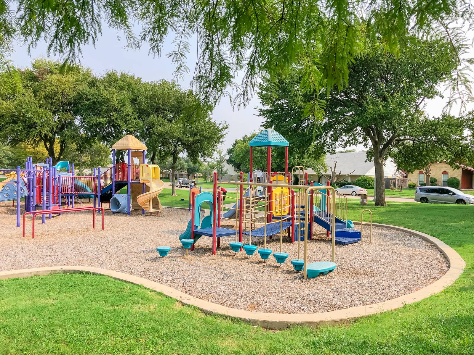 Colorful playground near residential neighborhood in Richardson, Texas, America. Community facility surrounded by large oak trees and green grass lawn