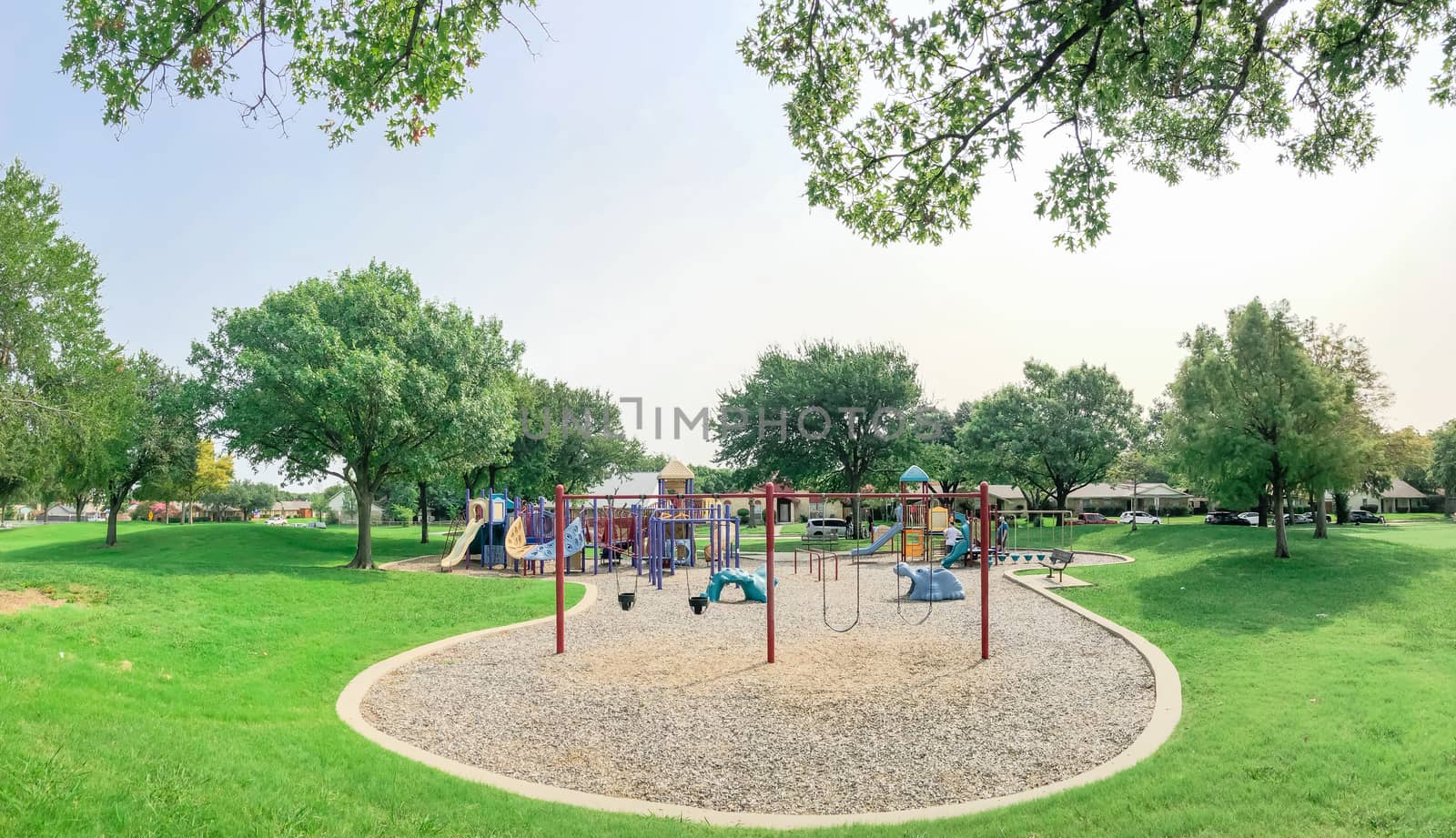 Panorama view colorful playground near residential neighborhood in Richardson, Texas, America. Community facility surrounded by large oak trees and green grass lawn