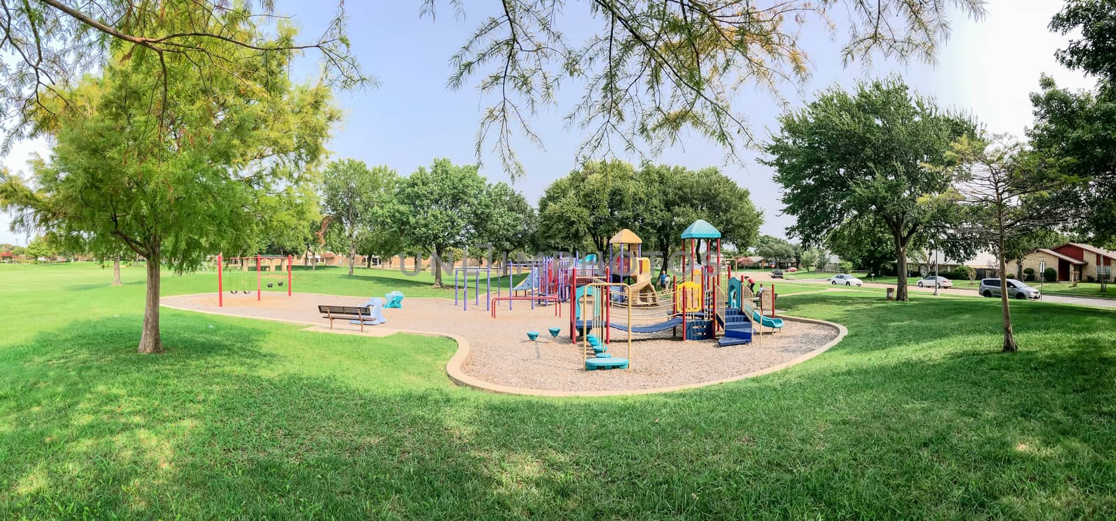 Panorama view colorful playground near residential neighborhood in Richardson, Texas, America. Community facility surrounded by large oak trees and green grass lawn