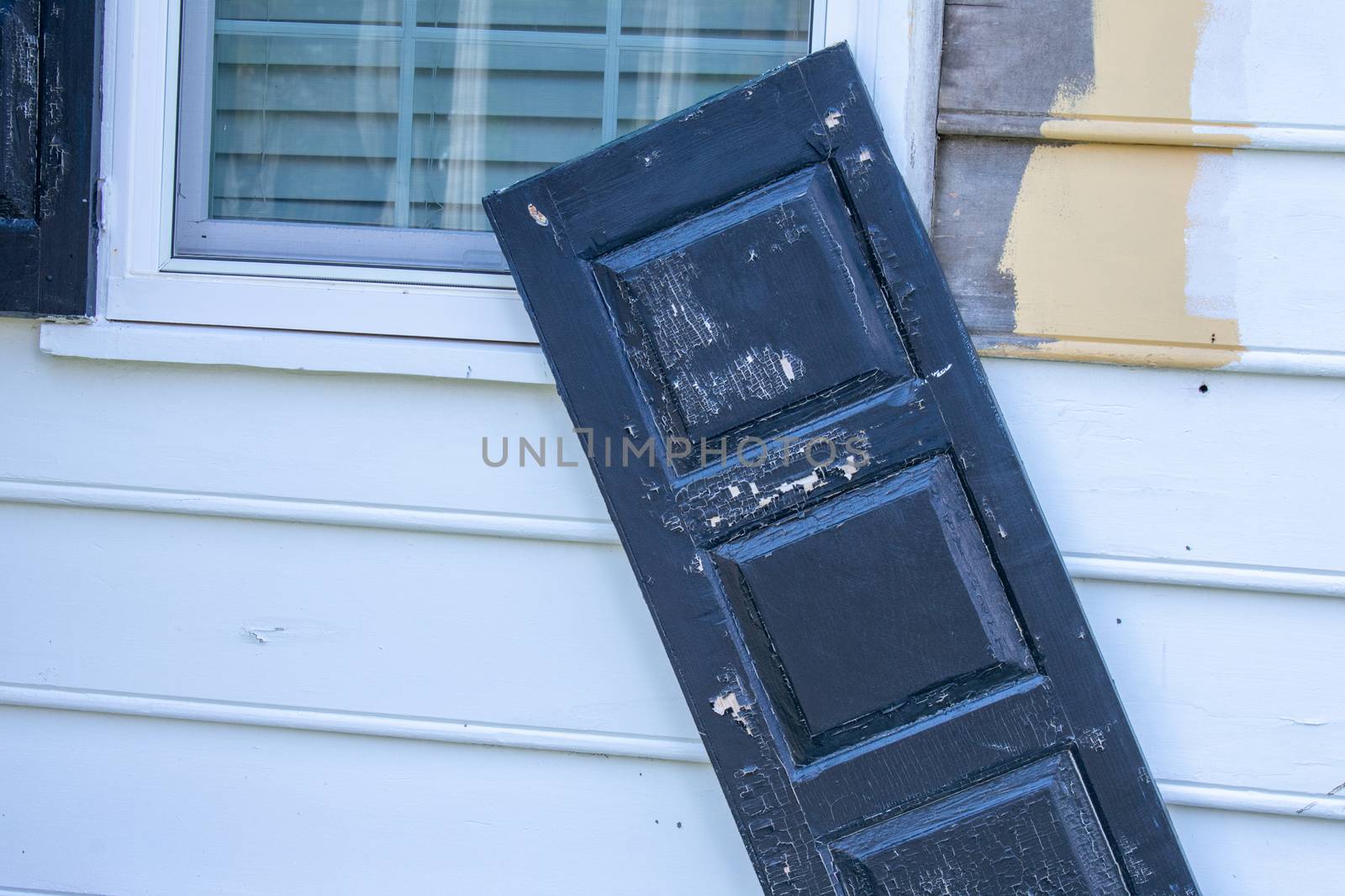 A Black Window Shutter Barely Hanging Onto the White Wall