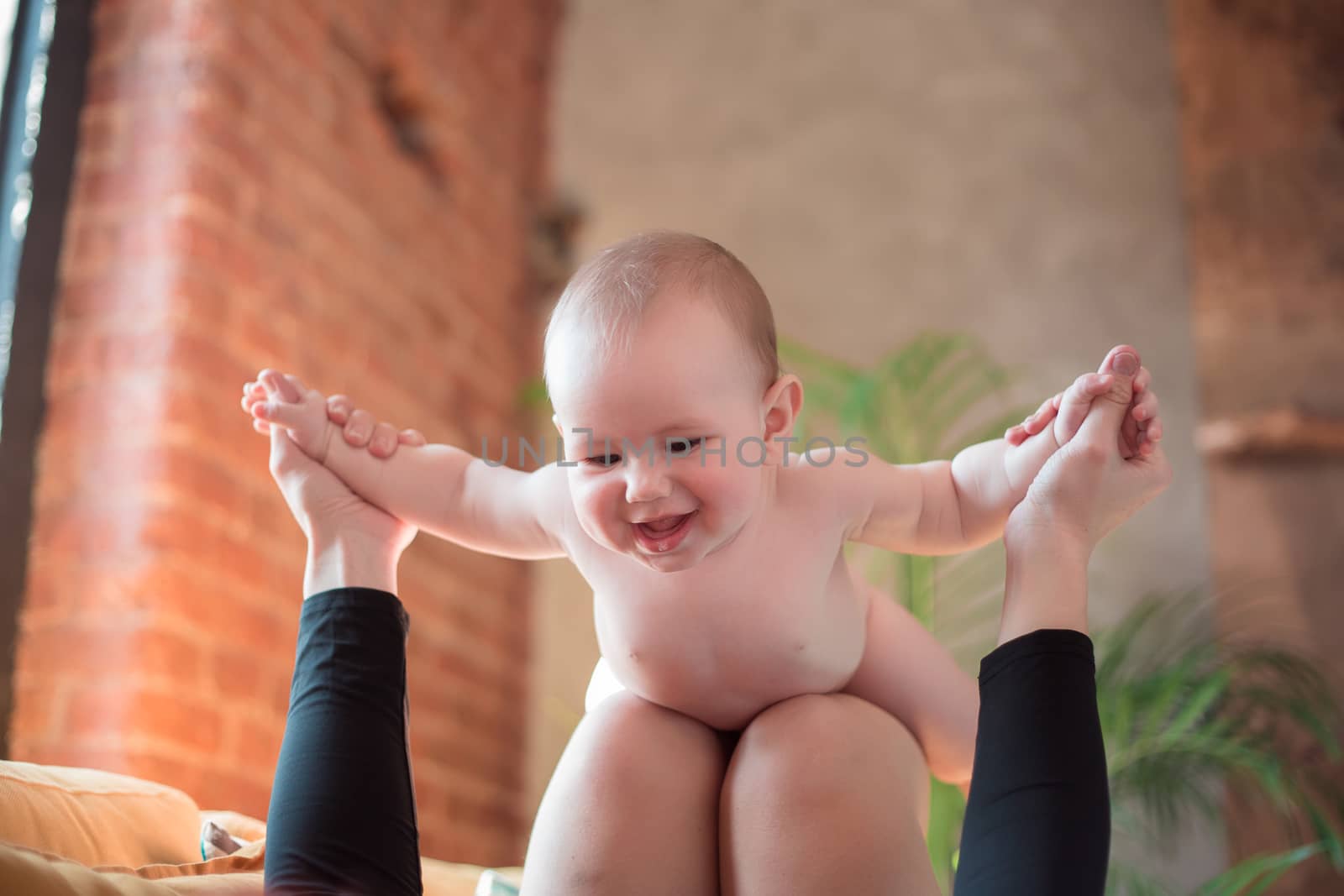 The baby lies on the lap of the mother in the airplane pose, the mother plays with the baby