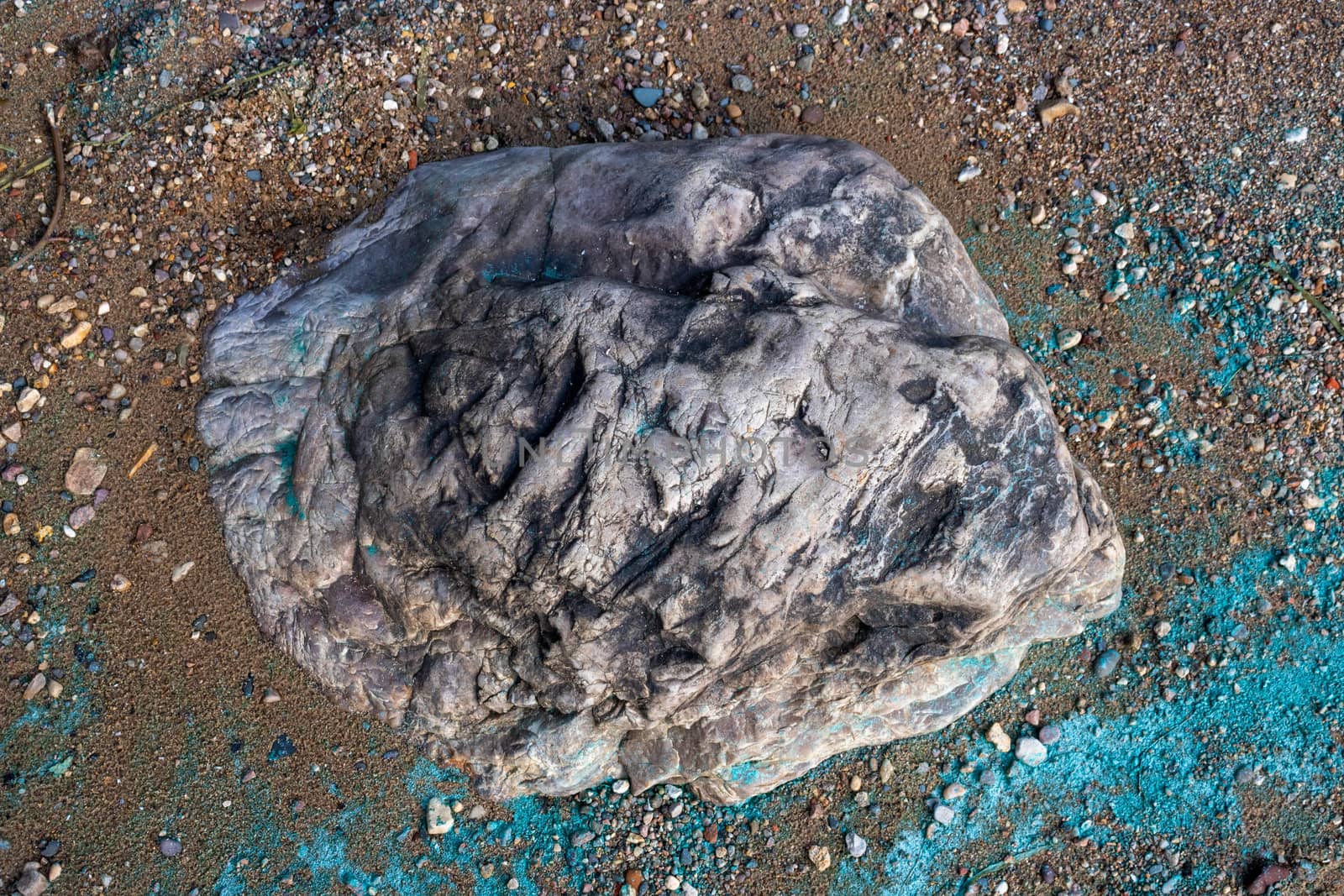 The stone lies in the sand on the coast.Nearby is a turquoise strip of river foam from the fuel.The concept of the environment.