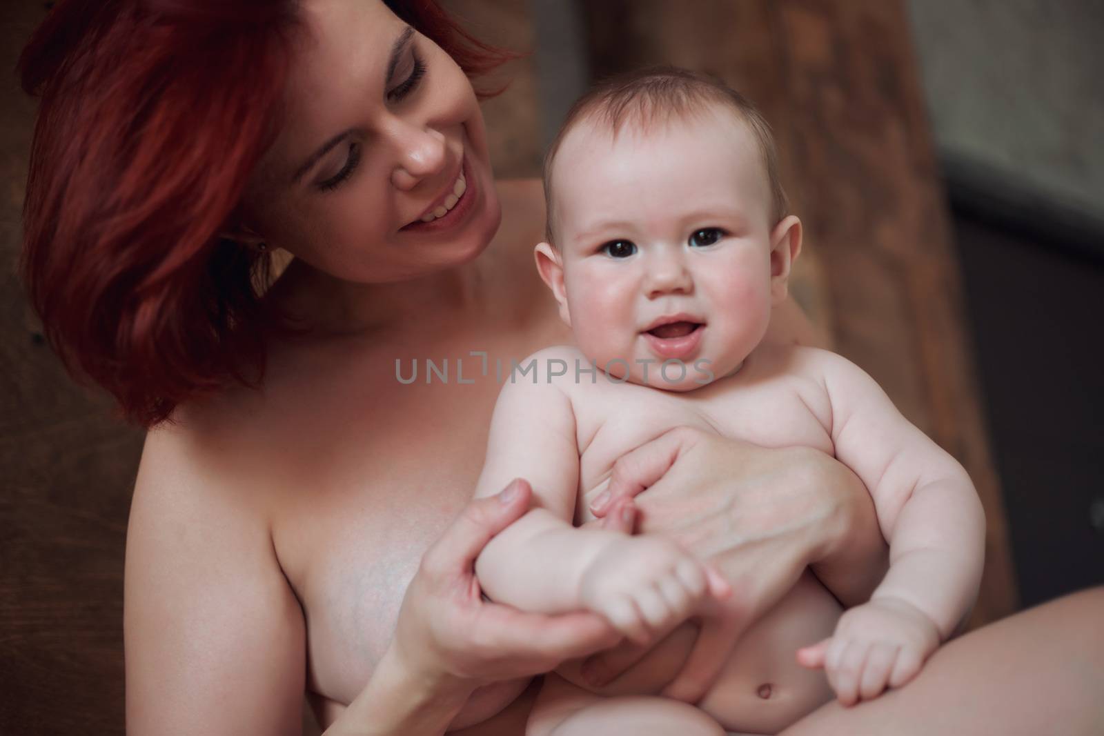 Mom holds the baby in her arms and looks at him tenderly, the baby smiles at the camera