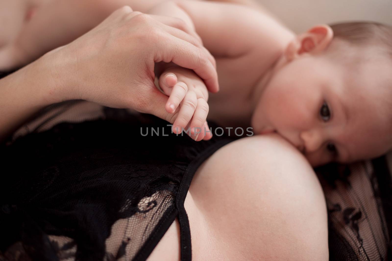 Mom holds the little hand of the baby boy in her hand while breastfeeding the baby