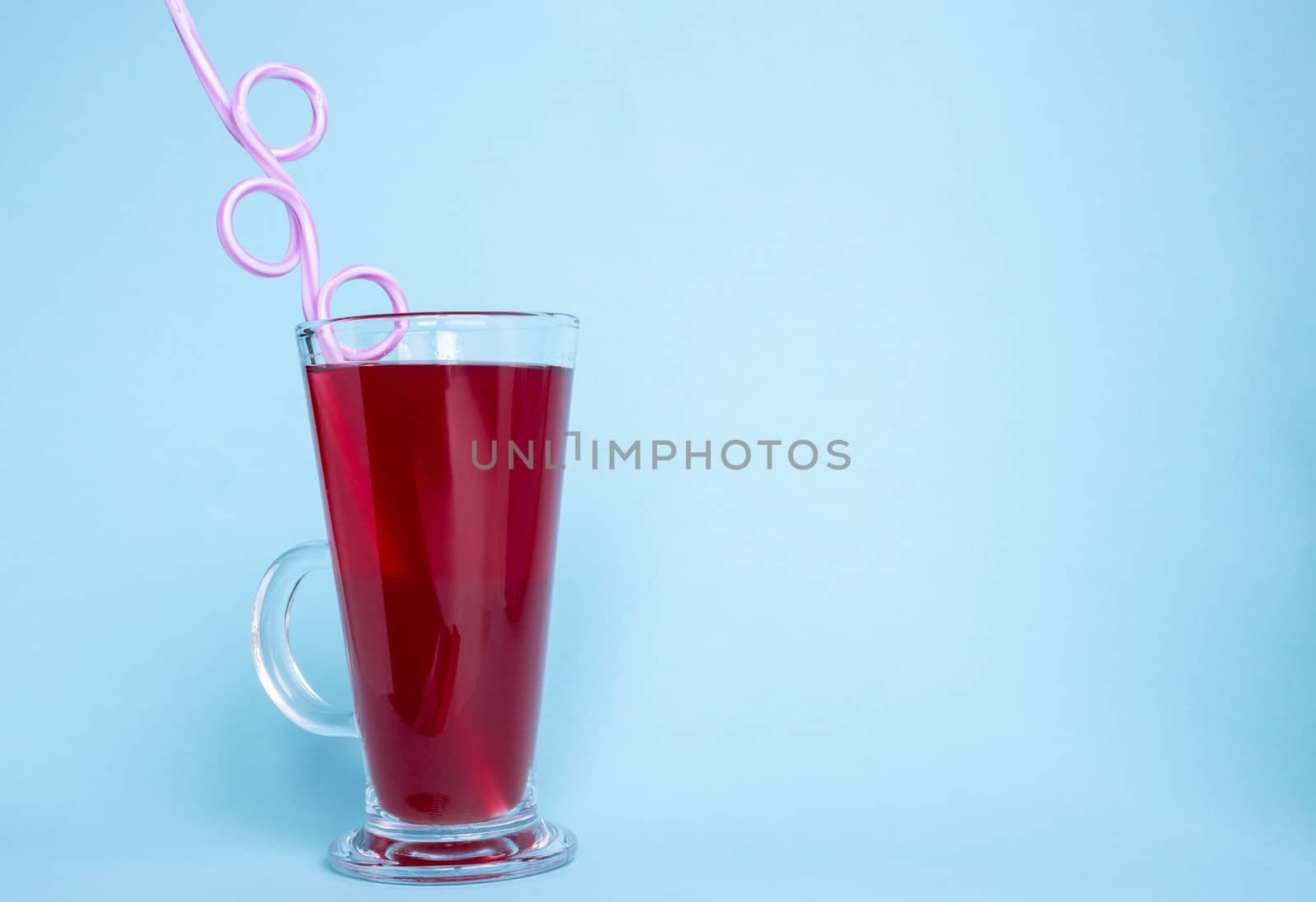 A glass with strawberry juice and a curved tube on a blue background. Space for your text by lapushka62