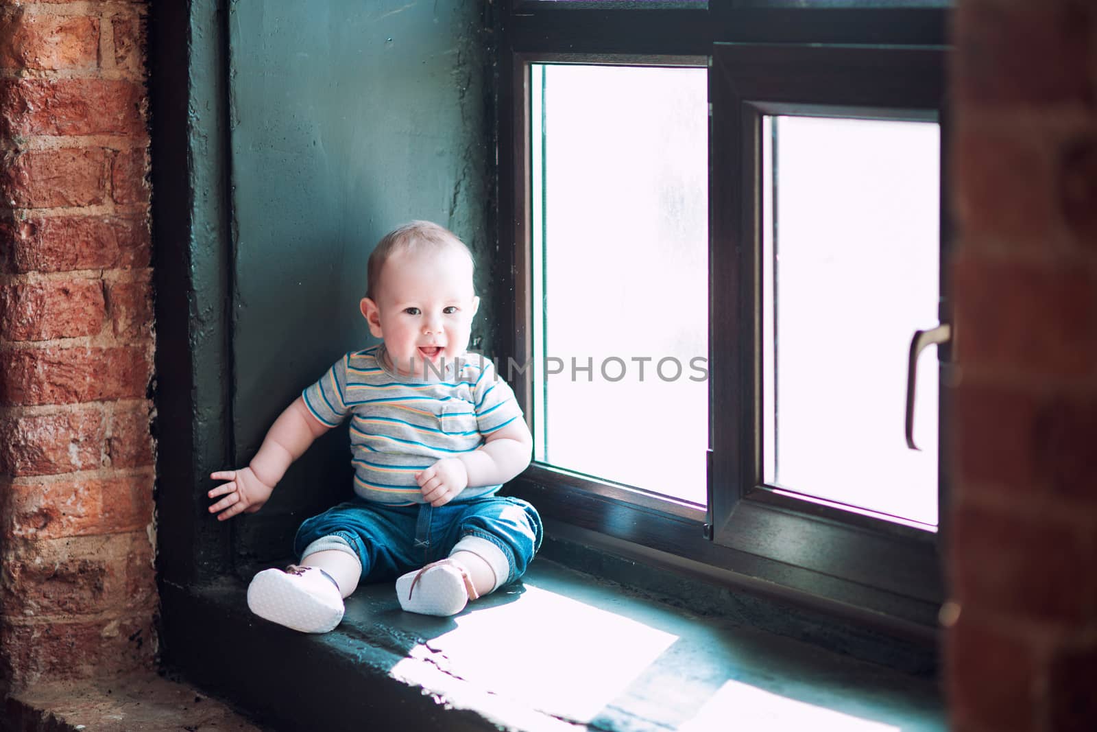 Little baby biy sits on the windowsill and smiles with all his mouth