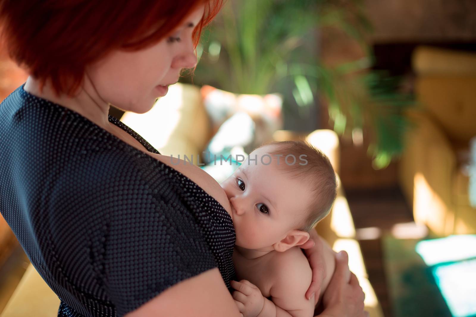 A young mother is breastfeeding her little child and looking at him tenderly