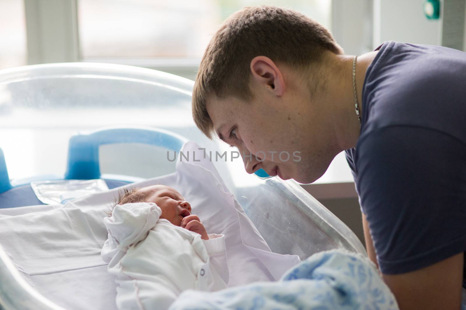 Beautiful newborn baby boy, laying in a small crib looking at his father finger in prenatal hospital