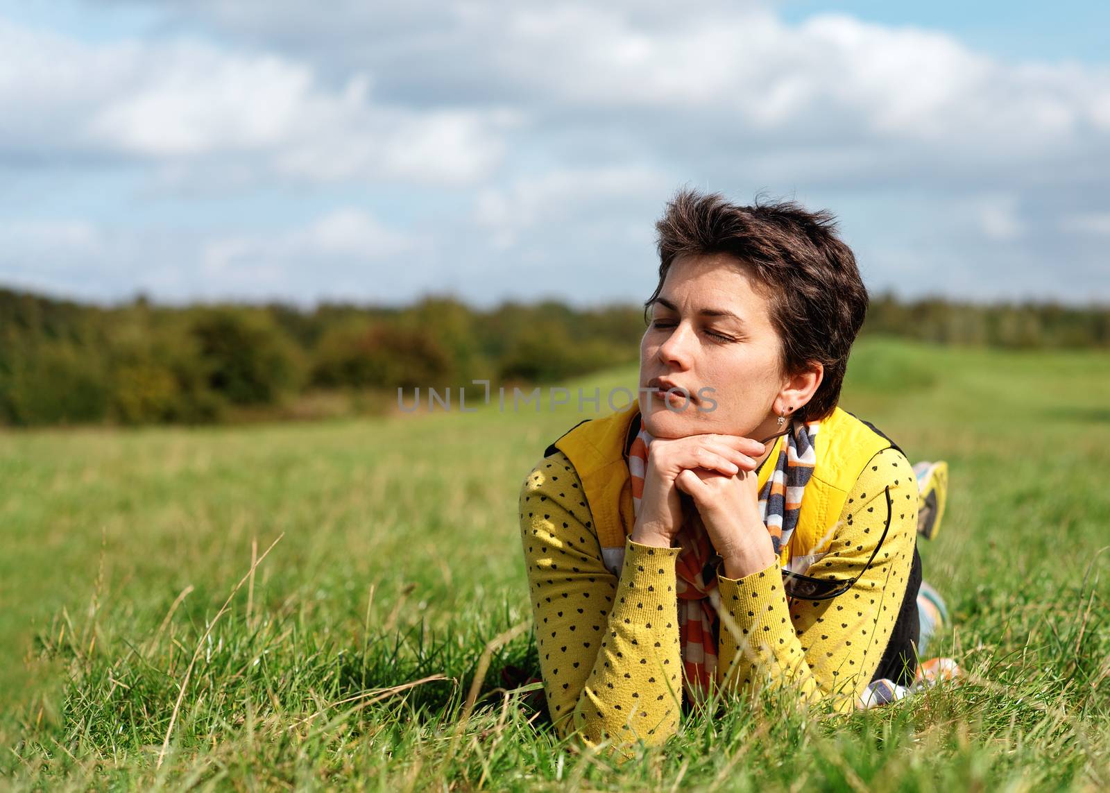 Woman wearing yellow coat and jeans lying on meadow on sunny sunny warm day in park