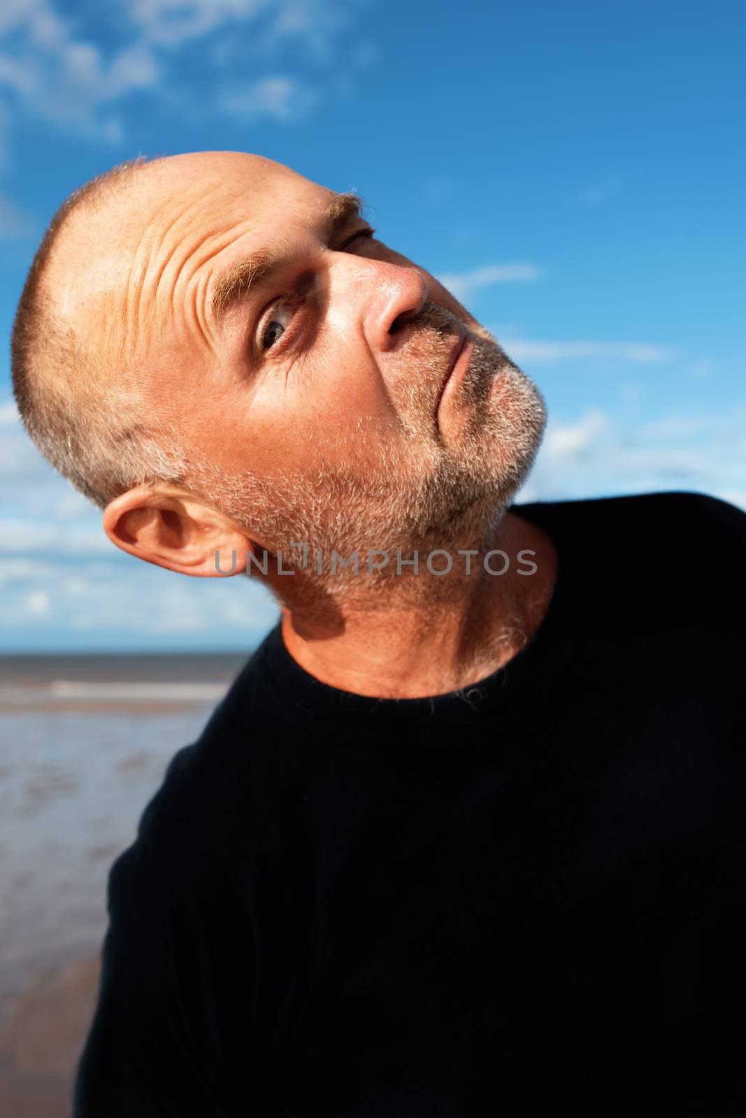 the man in black t-shirt winking and looking into the camera at the seaside
