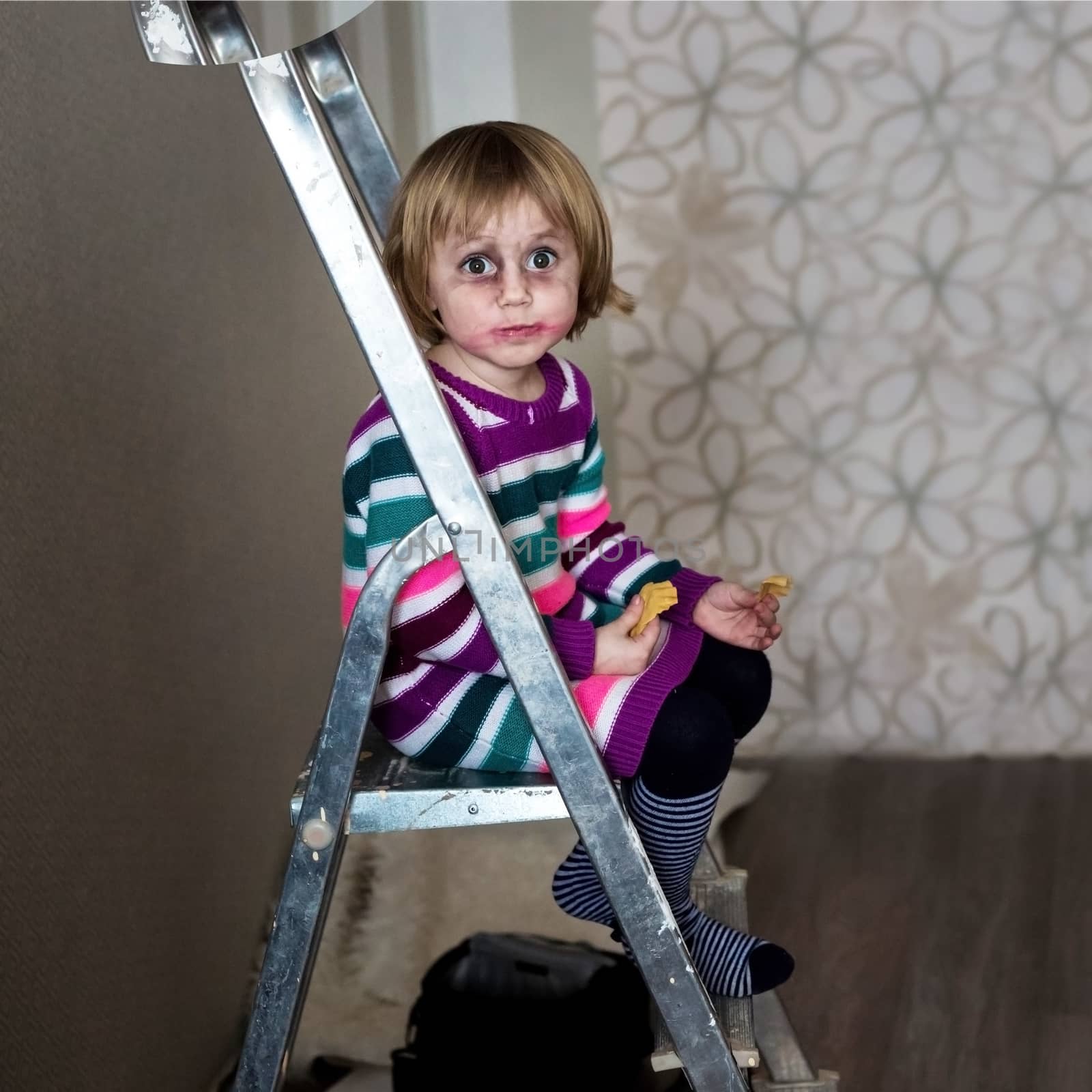 Cheerful little girl having fun sits on a stepladder and smiles. by galinasharapova