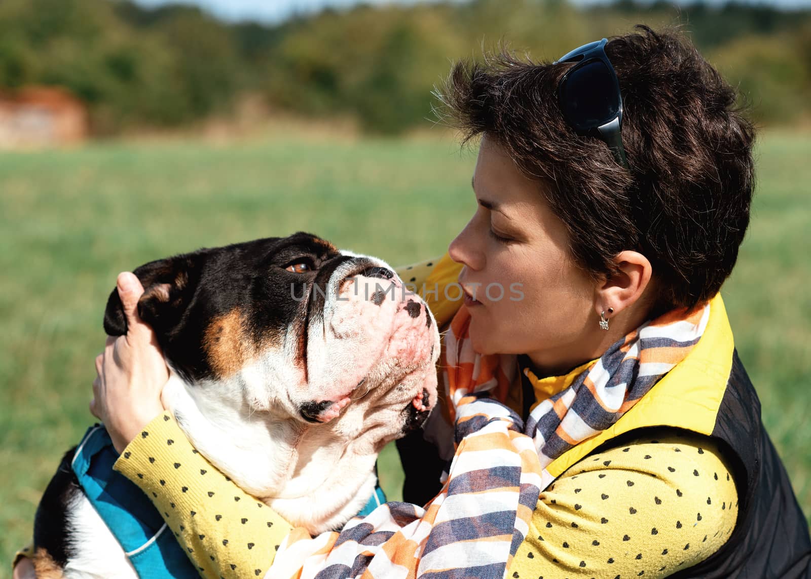 a woman and an English bulldog hugging in a clearing on a warm summer day