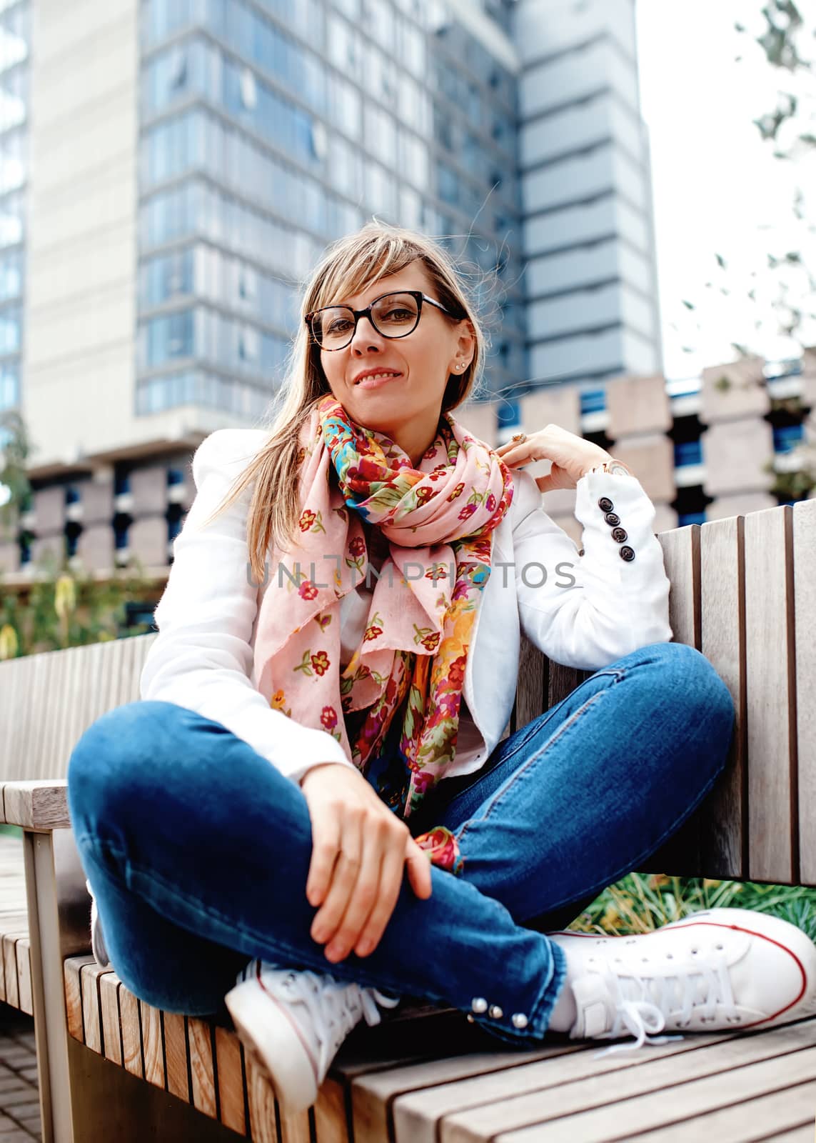 woman sitting on bench in city centre against skyscraper
