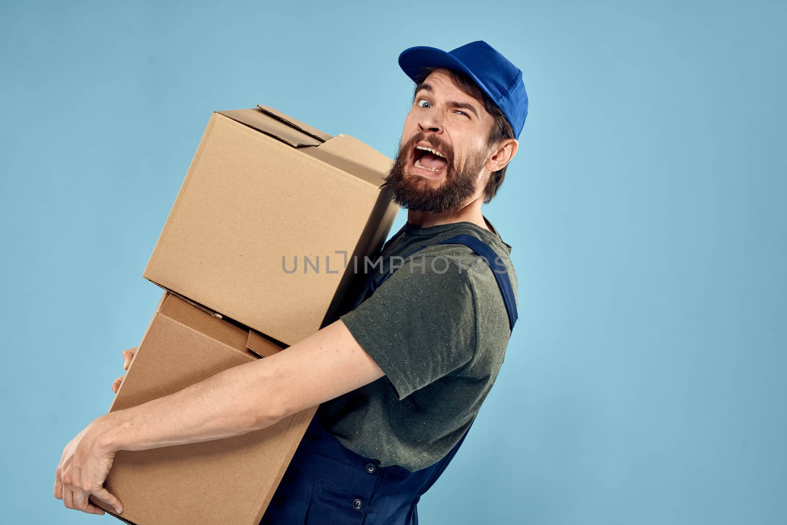 Man in working uniform with boxes in hands delivery service blue background by SHOTPRIME
