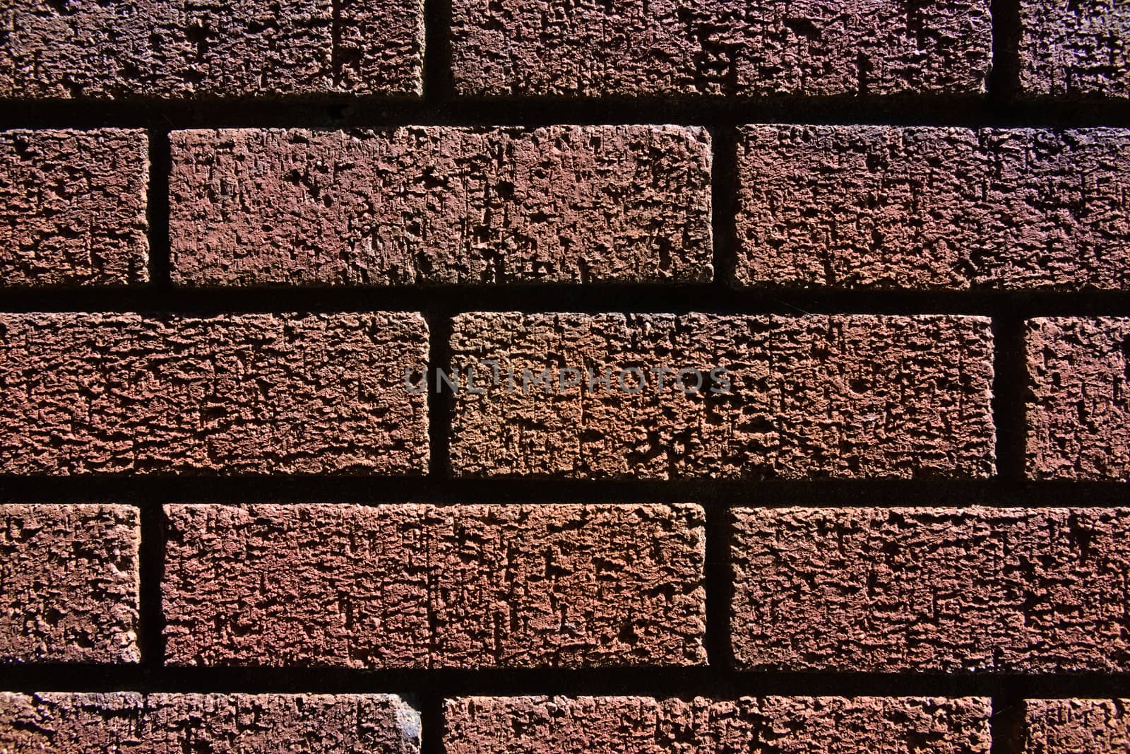 2 - Abstract texture close up of a red brick wall shadows and bright highlights make contrasted image. Fine grain and structure visible. Horizontal.