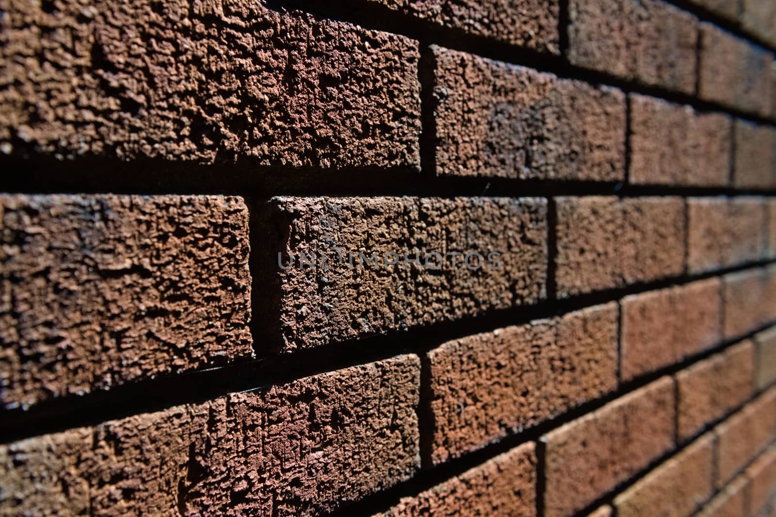 4 - Abstract selective focus side view of harshly lit red brick wall. Lines converge into the blurred distance. Lit by bright sunlight.