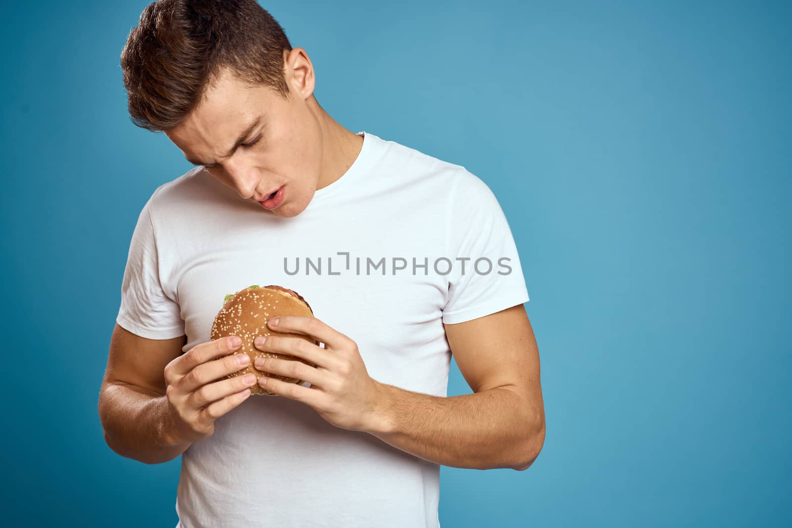 man with hamburger and white t-shirt blue background emotions gesturing with hands Copy Space by SHOTPRIME