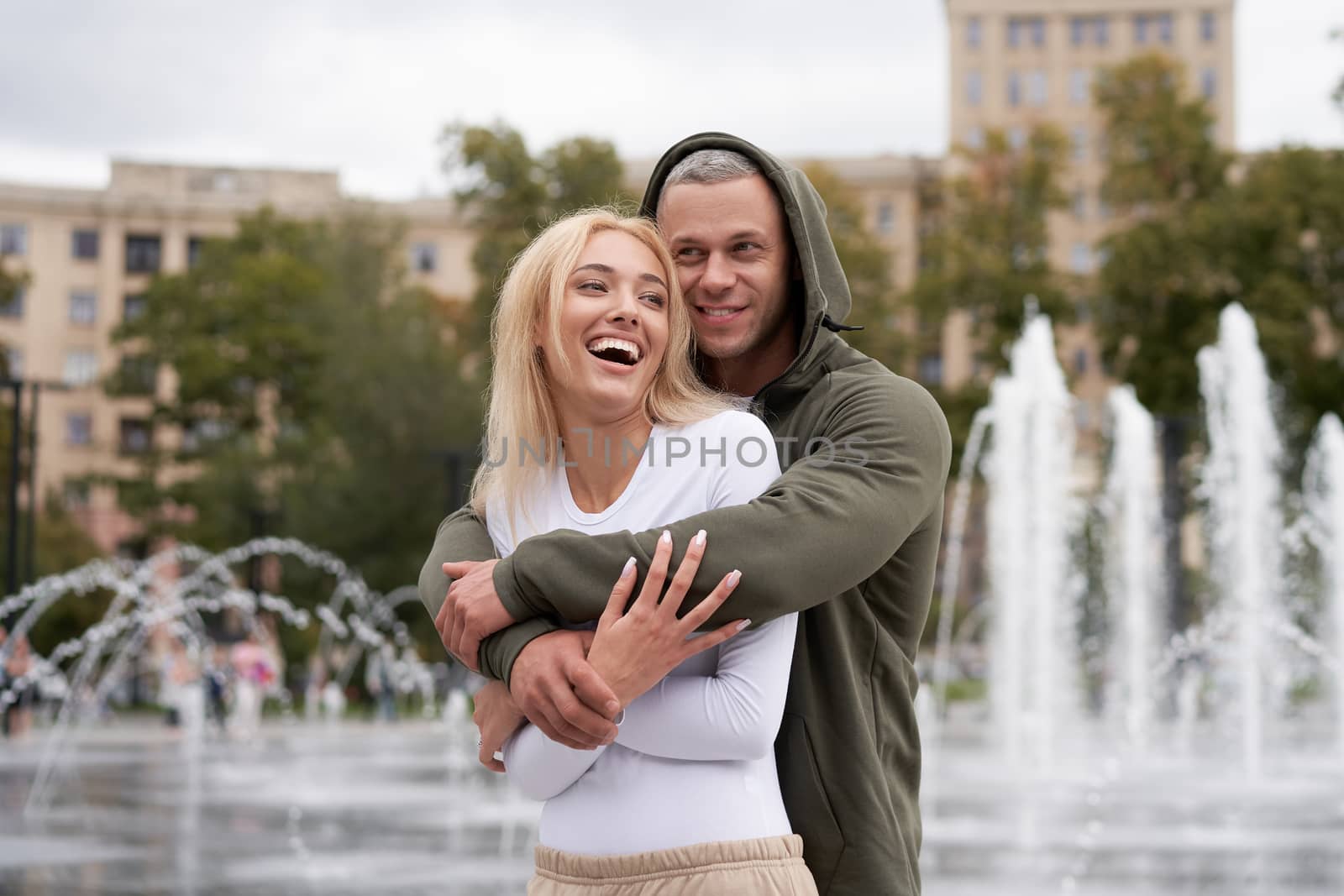 Couple in love walking outdoors park fountain Caucasian man woman walk outside after jogging dressed sport clothes Healthy livestyle dress up the hood