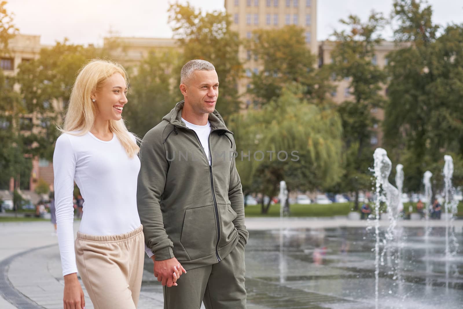 Couple in love walking outdoors park fountain Caucasian man woman walk outside after jogging dressed sport clothes Healthy livestyle Hold hands each other