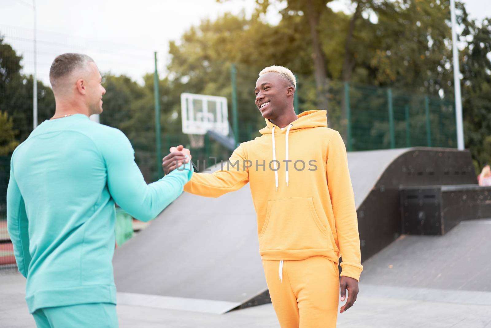 Multi-ethnic friendship Black african-american and caucasian guy friends spending time together on skate park Two multi ethnic student Dressed colorful sportswear shaking hands each other.