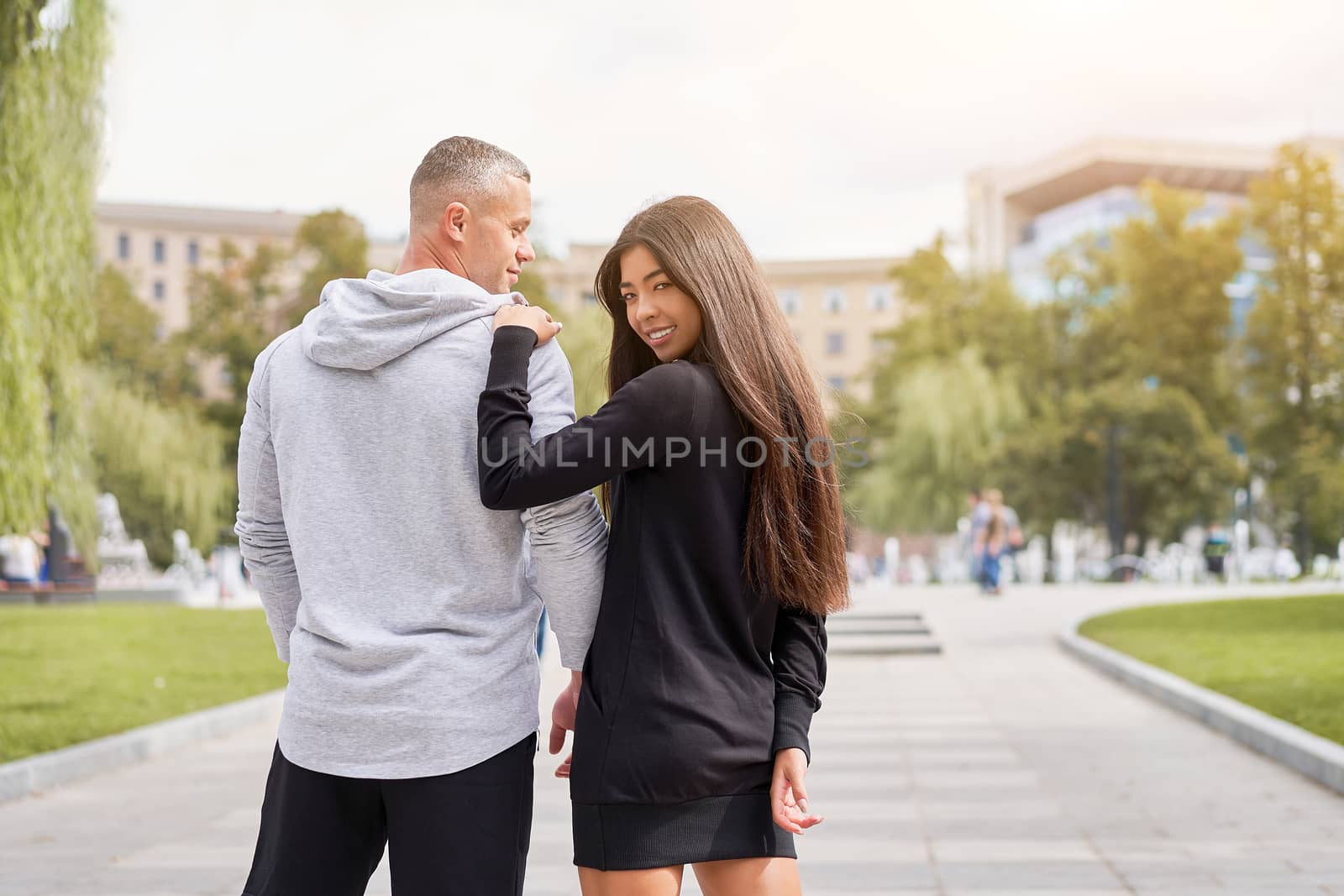 Couple in love walking outdoors park fountain Caucasian man asian woman walk outside dressed sport clothes Rear view