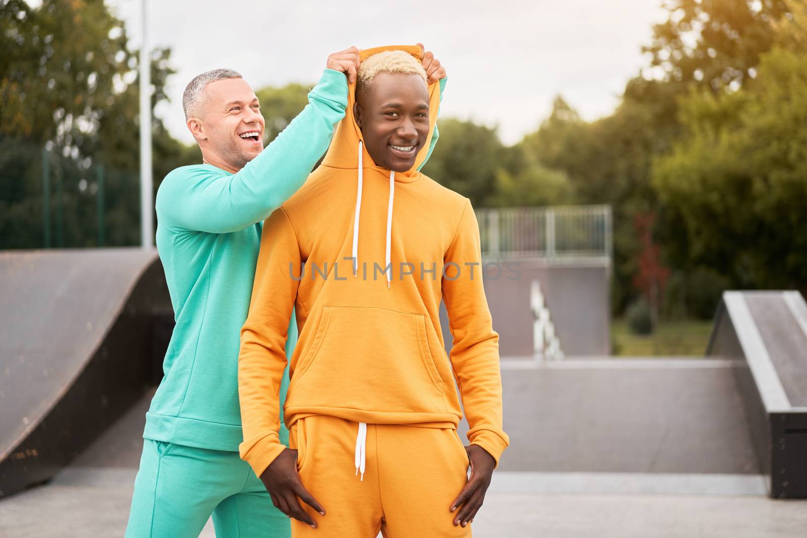 Multi-ethnic friendship Black african-american and caucasian guy friends spending time together on skate park Two multi ethnic student Dressed colorful sportswear.